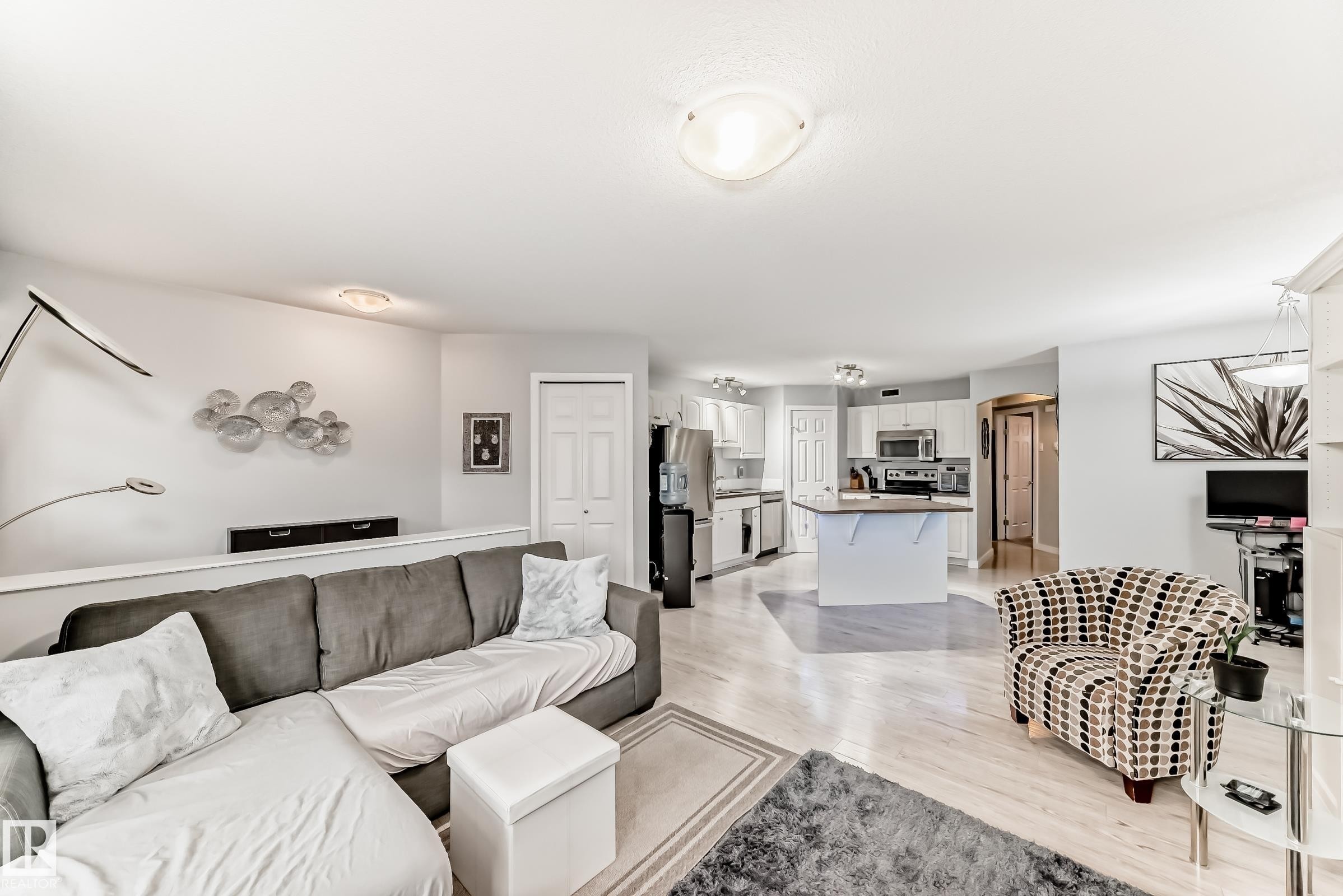 Open-concept living space featuring wood-finish flooring, recessed lighting, white walls, and a kitchen with white cabinetry and stainless steel appliances - 53 150 Edwards Drive, Edmonton, AB