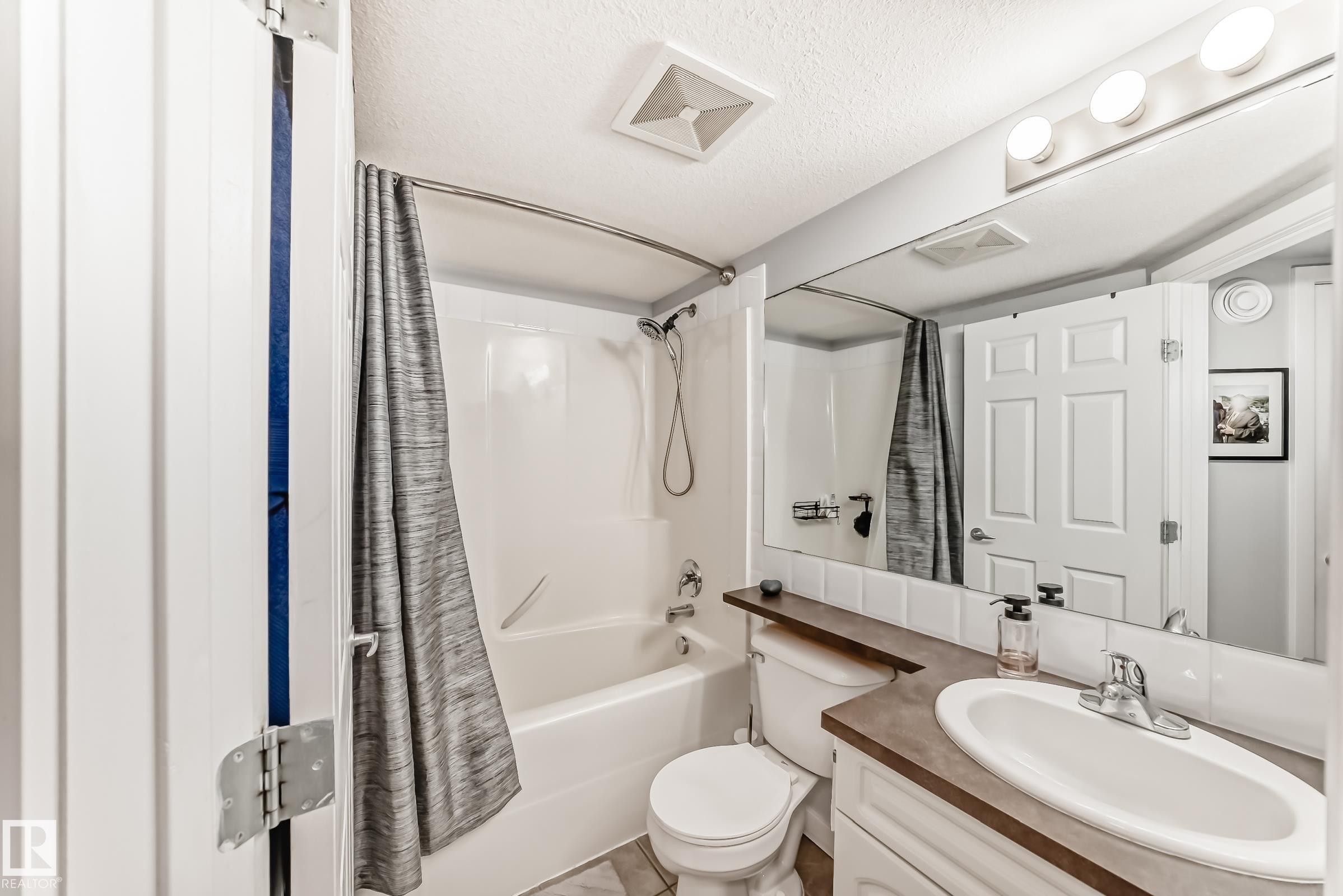 Bathroom featuring a white bathtub, ceramic tile flooring, built-in vanity with a wood-finish countertop, and an integrated basin - 53 150 Edwards Drive, Edmonton, AB