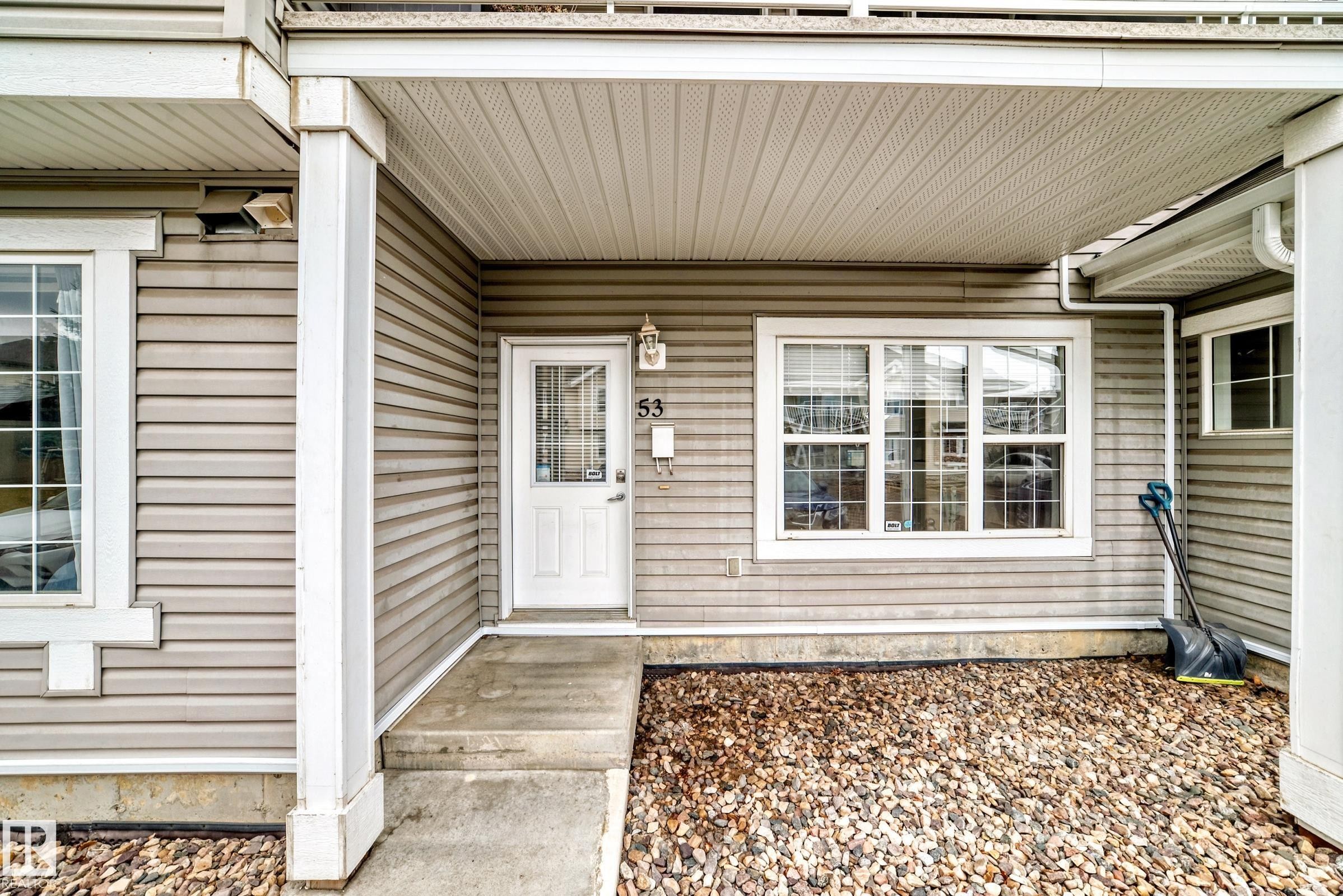 Front entry featuring a white door with upper glass panel, an exterior light fixture, and a house number - 53 150 Edwards Drive, Edmonton, AB