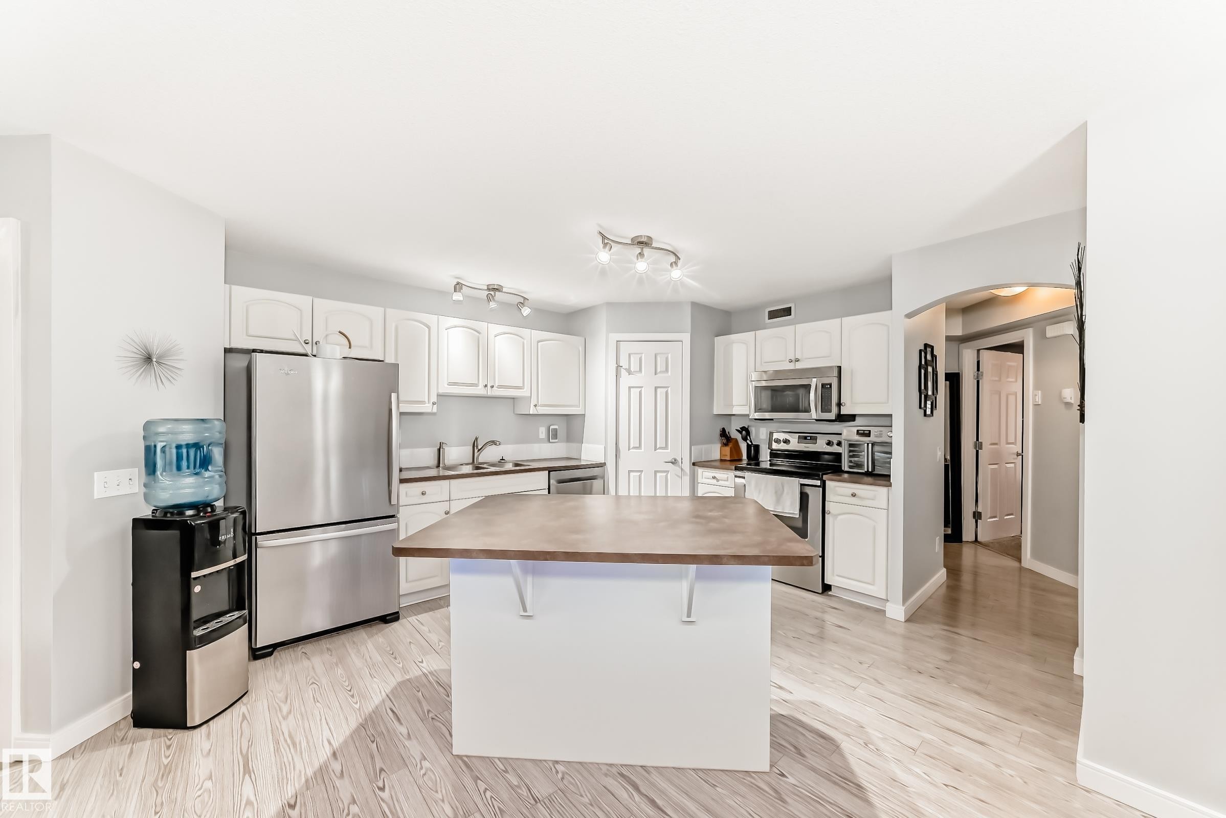 Open-concept kitchen featuring an island with a wood-finish countertop, white cabinetry, stainless steel appliances, and light wood-finish flooring - 53 150 Edwards Drive, Edmonton, AB
