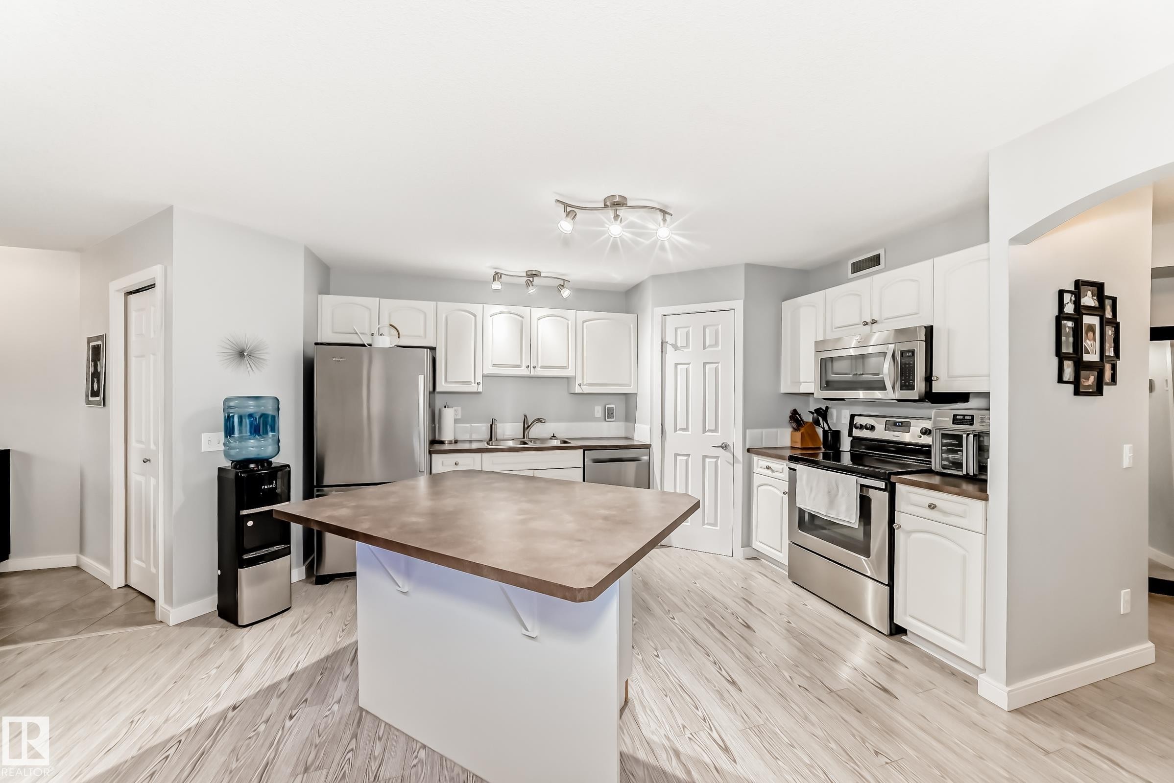 Kitchen featuring a central island, white cabinetry, stainless steel appliances, wood-finish flooring, and recessed lighting - 53 150 Edwards Drive, Edmonton, AB