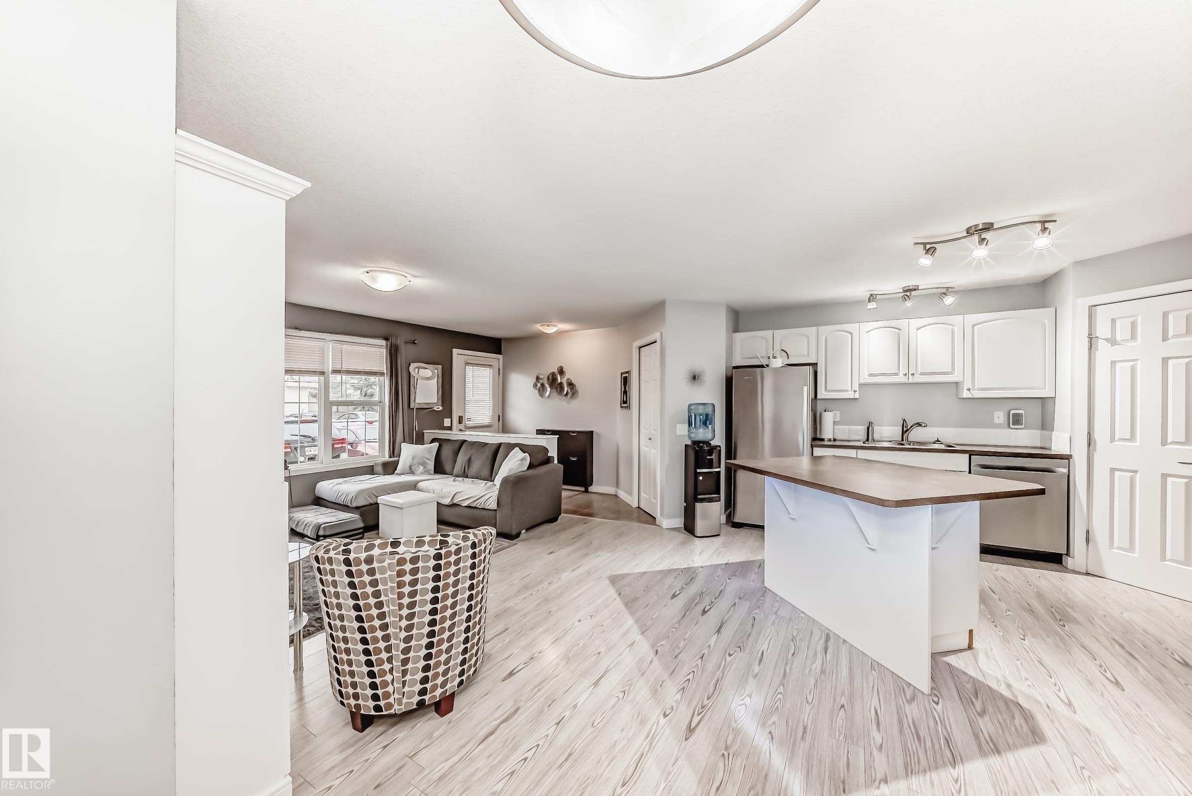 Open-concept living space featuring wood-finish flooring, a kitchen island with a wood-finish countertop, white cabinetry, stainless steel appliances, and track lighting - 53 150 Edwards Drive, Edmonton, AB