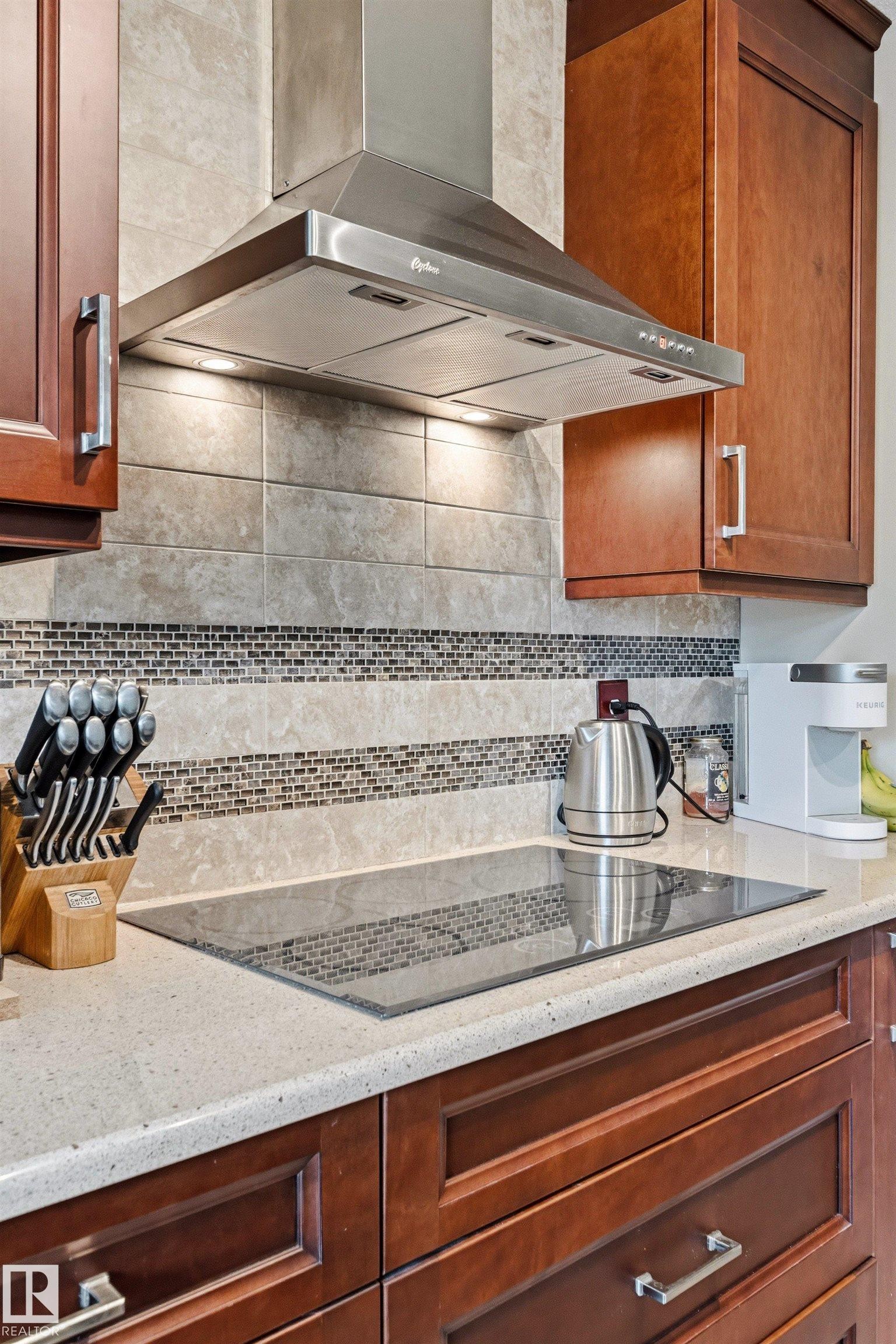 Stainless steel range hood with integrated lighting over a sleek induction cooktop - 32 Lamplight Bay, Spruce Grove, AB