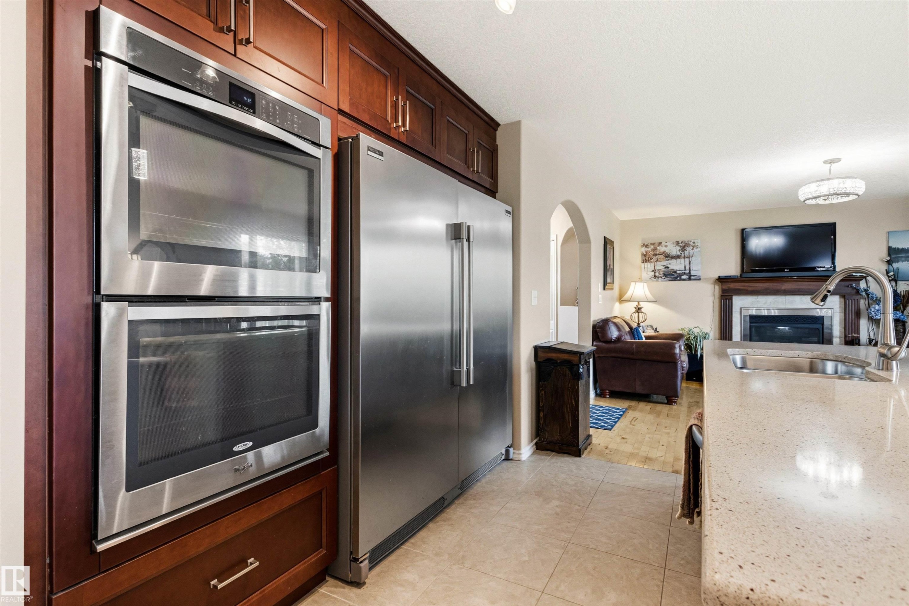 Kitchen appliances featuring stainless steel double ovens and a full-size refrigerator, complemented by rich wood cabinetry - 32 Lamplight Bay, Spruce Grove, AB