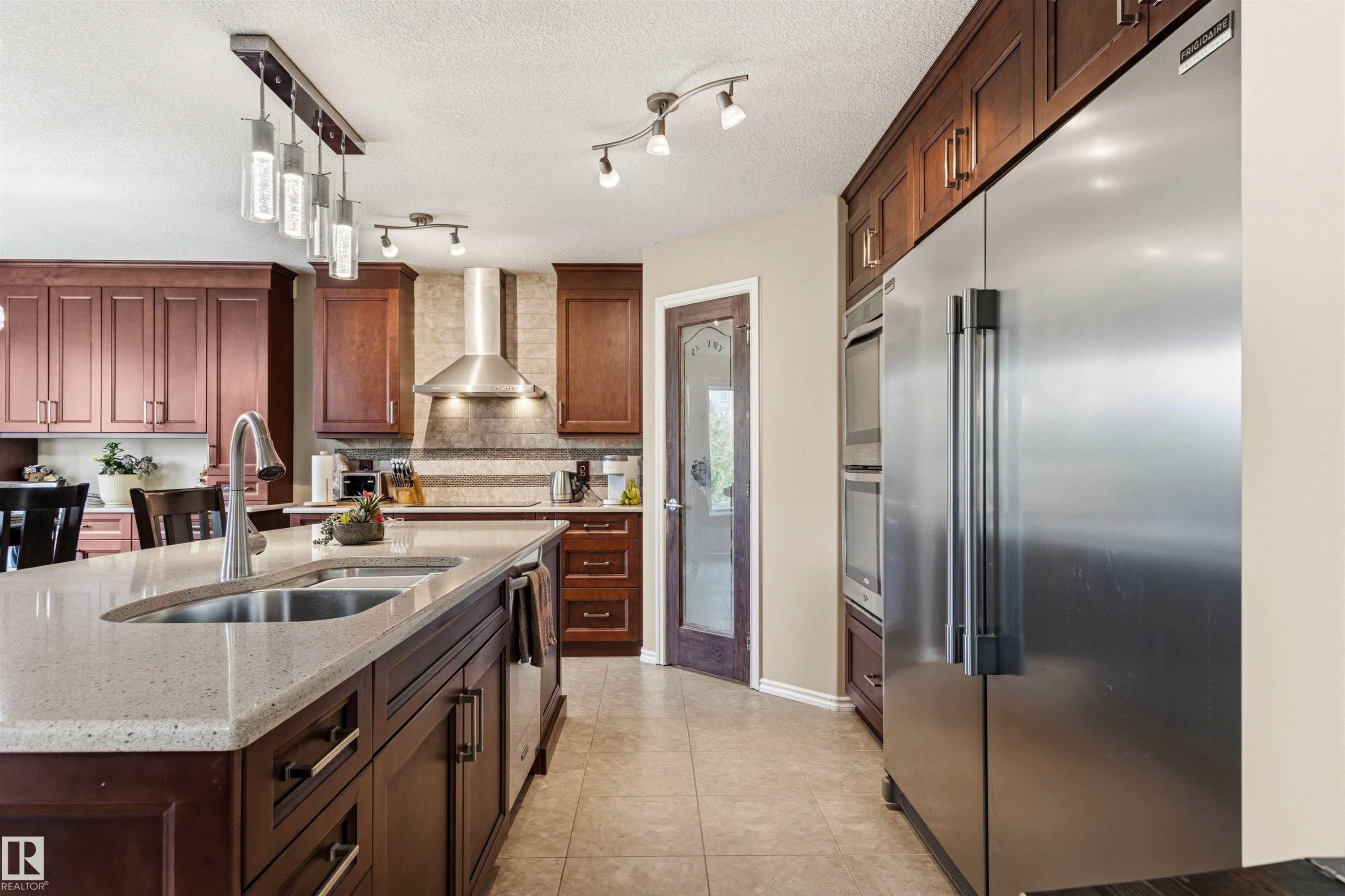 Spacious kitchen featuring a large island with an undermount sink, rich wood cabinetry, stainless steel appliances, a tiled backsplash, and recessed lighting - 32 Lamplight Bay, Spruce Grove, AB