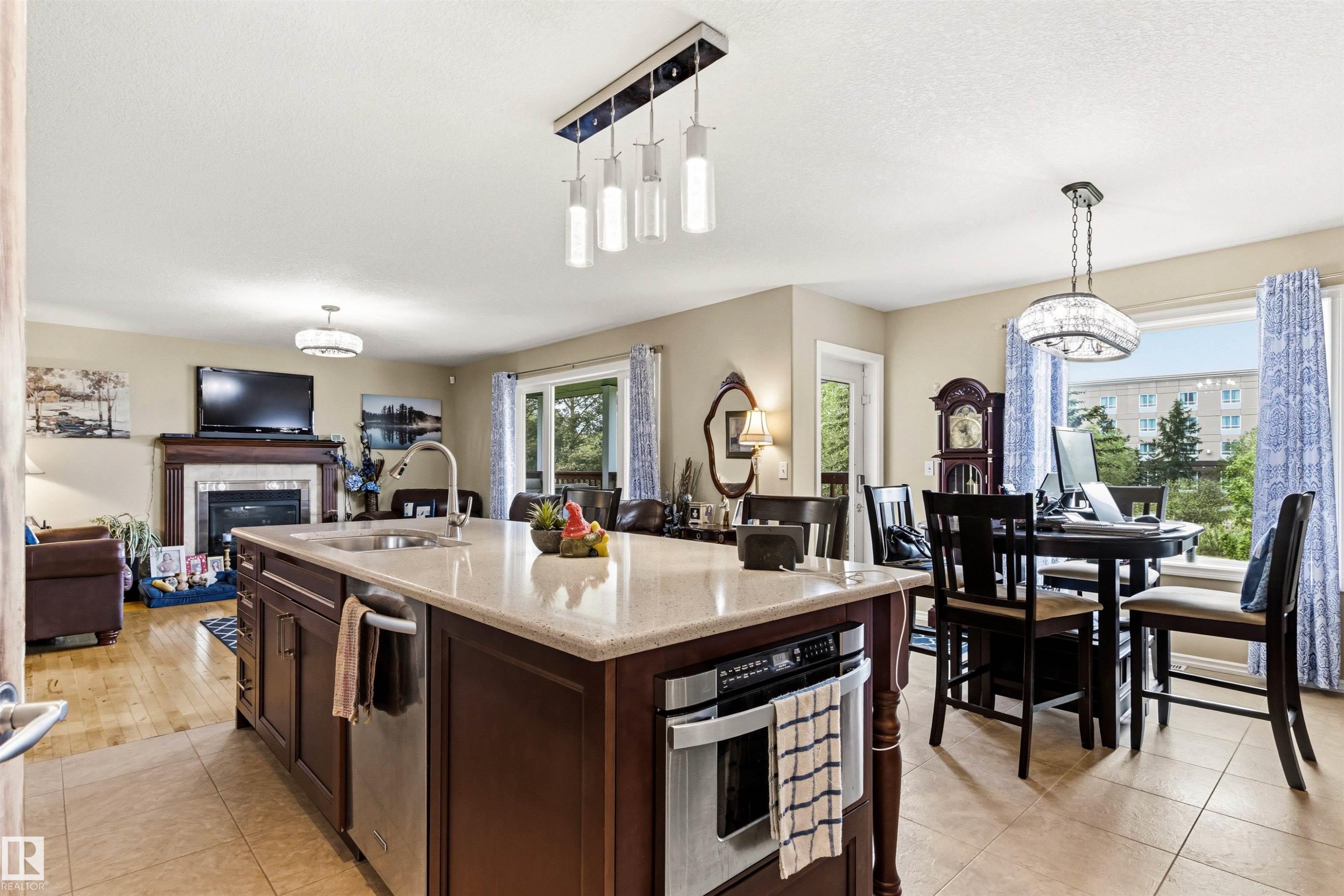 Open-concept kitchen and living area featuring a large center island with integrated sink and dishwasher, light-toned countertop, and recessed microwave - 32 Lamplight Bay, Spruce Grove, AB