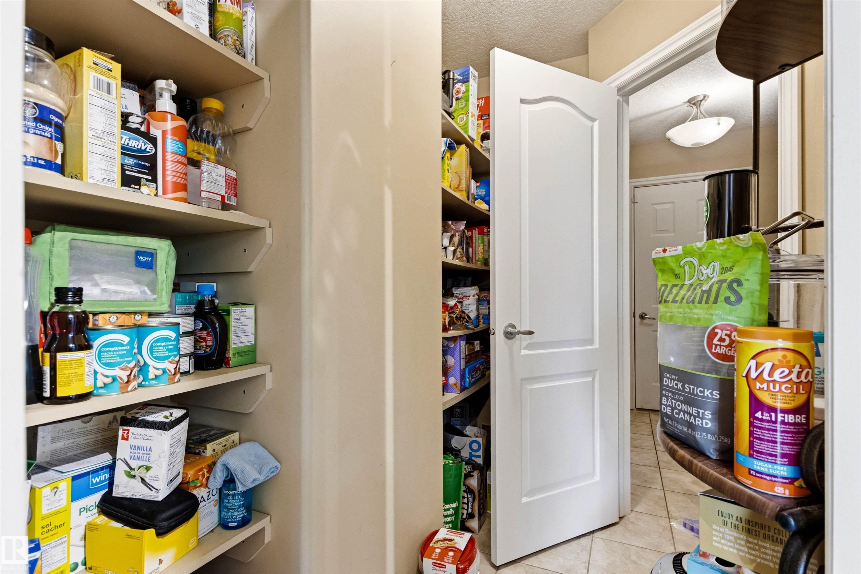 Kitchen pantry featuring extensive built-in shelving, a solid white door, and tiled flooring - 32 Lamplight Bay, Spruce Grove, AB