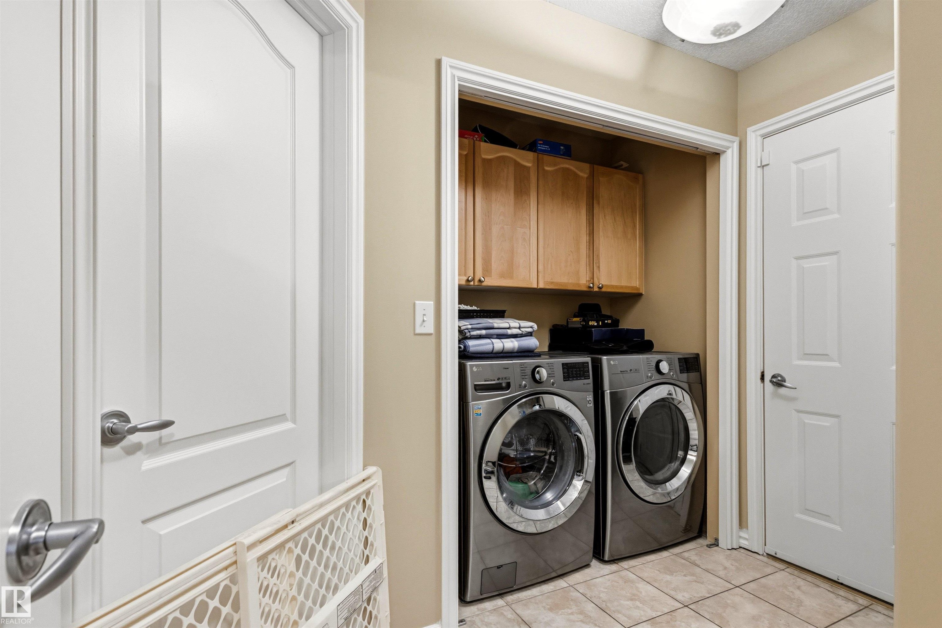 Dedicated laundry area featuring front-loading appliances, upper cabinetry for storage, and light-toned tile flooring - 32 Lamplight Bay, Spruce Grove, AB