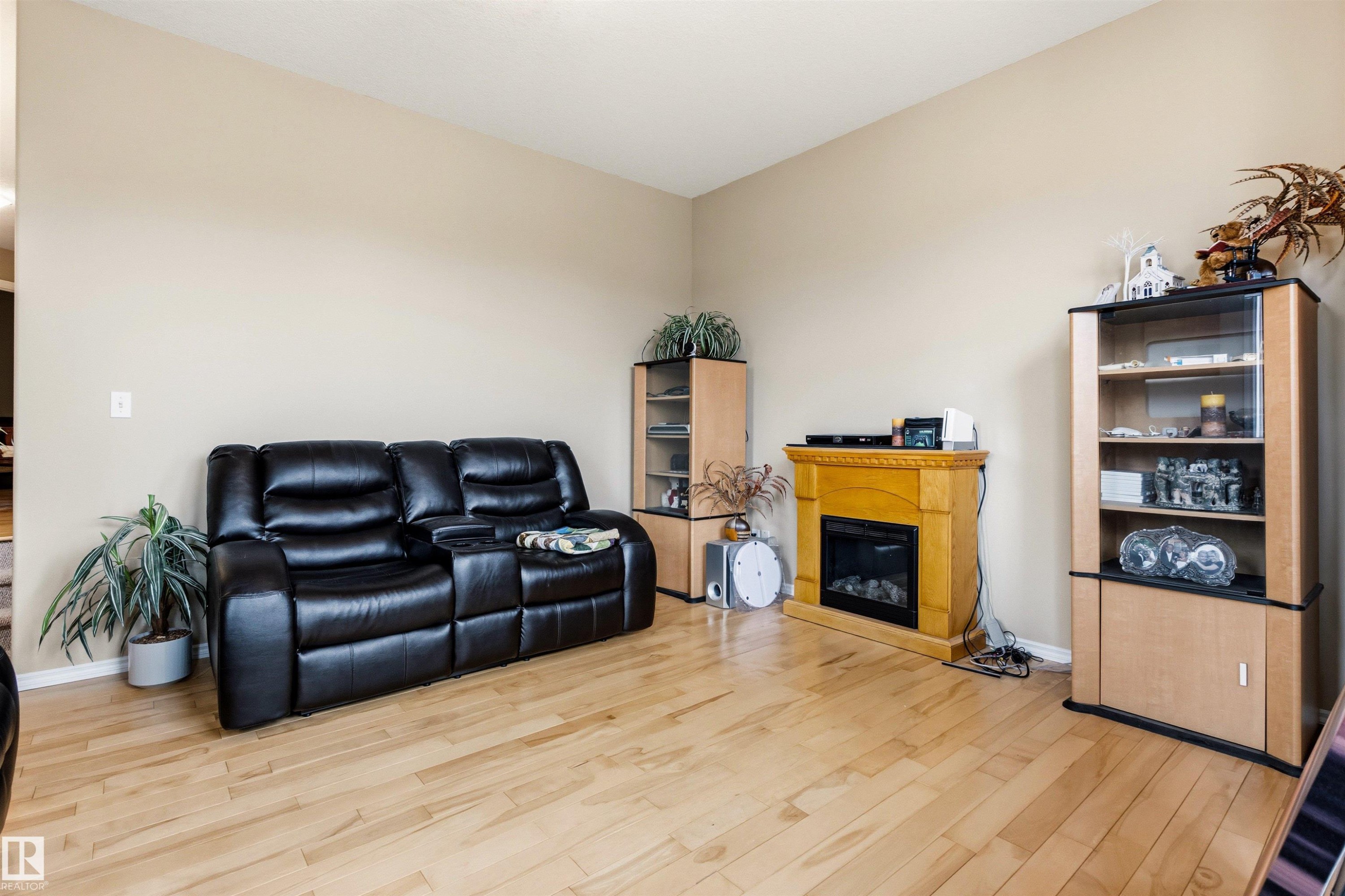 Spacious room featuring light wood-finish flooring, neutral wall tones, and a built-in fireplace with a wooden mantel - 32 Lamplight Bay, Spruce Grove, AB