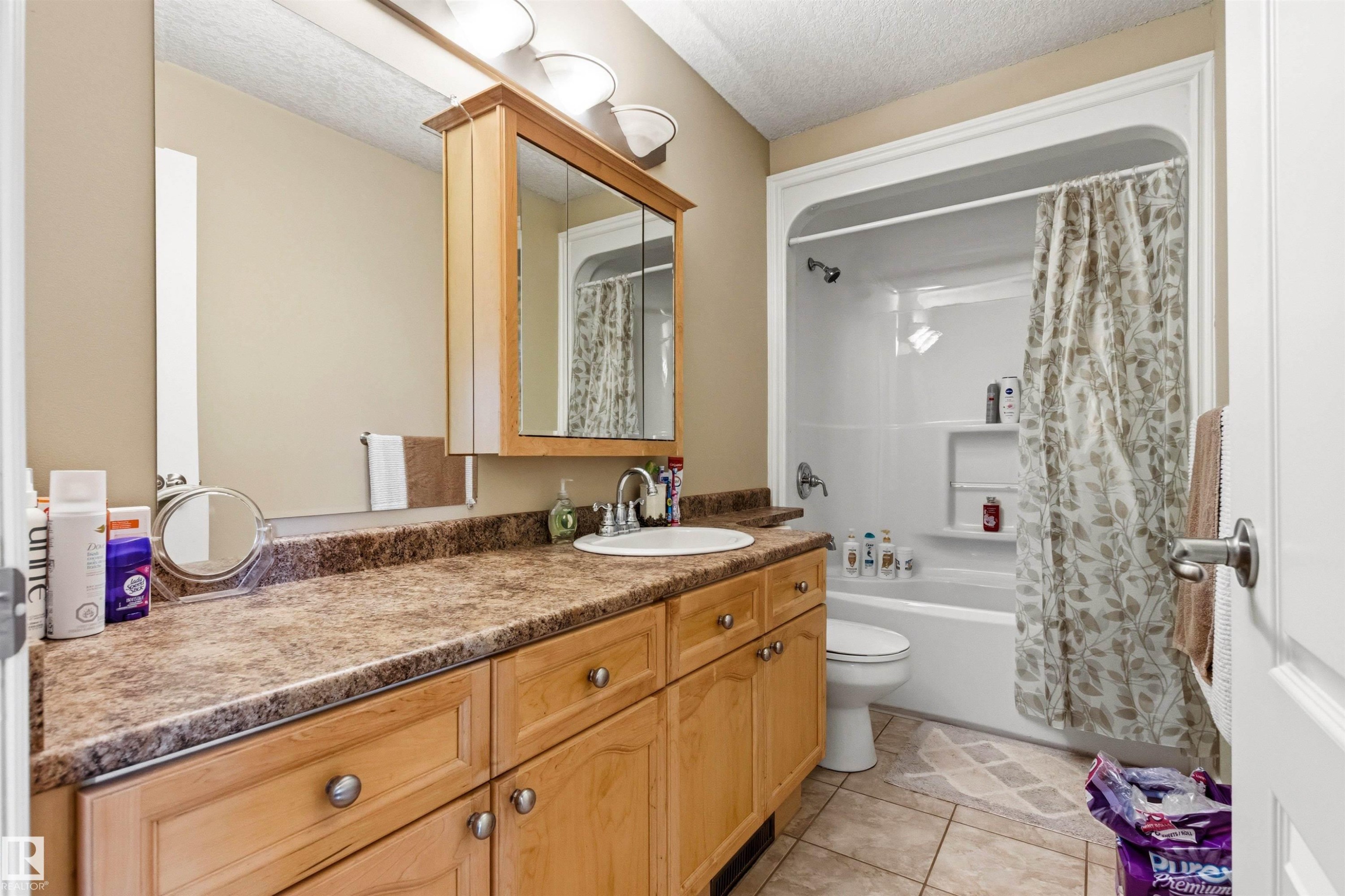 Bathroom featuring a wood-finish vanity with a built-in sink, a laminate countertop, and a medicine cabinet with integrated lighting - 32 Lamplight Bay, Spruce Grove, AB