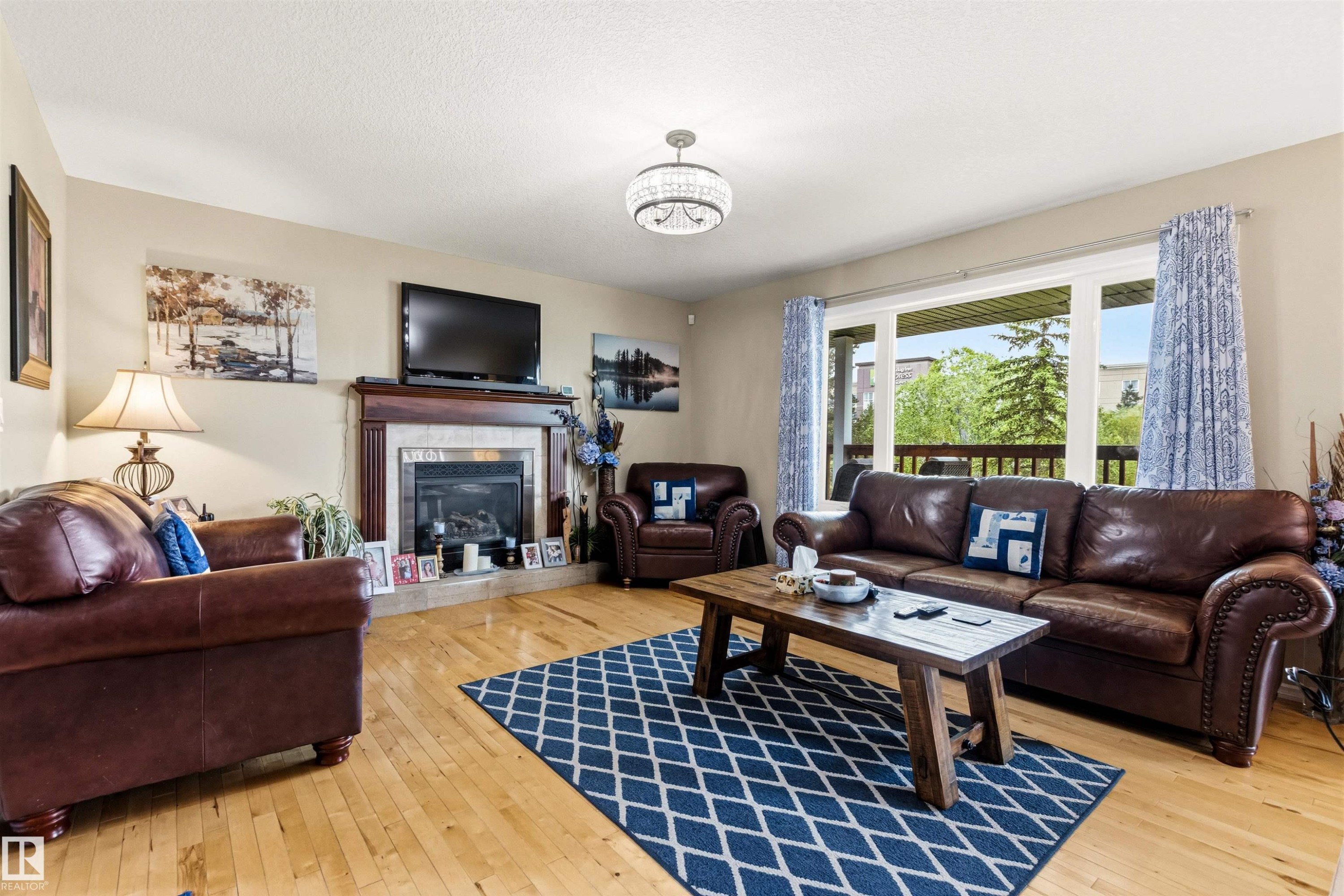 Living area featuring wood-finish flooring, a fireplace with a wood mantel and tile surround, and a large sliding glass door opening to a private balcony with a wooden railing - 32 Lamplight Bay, Spruce Grove, AB
