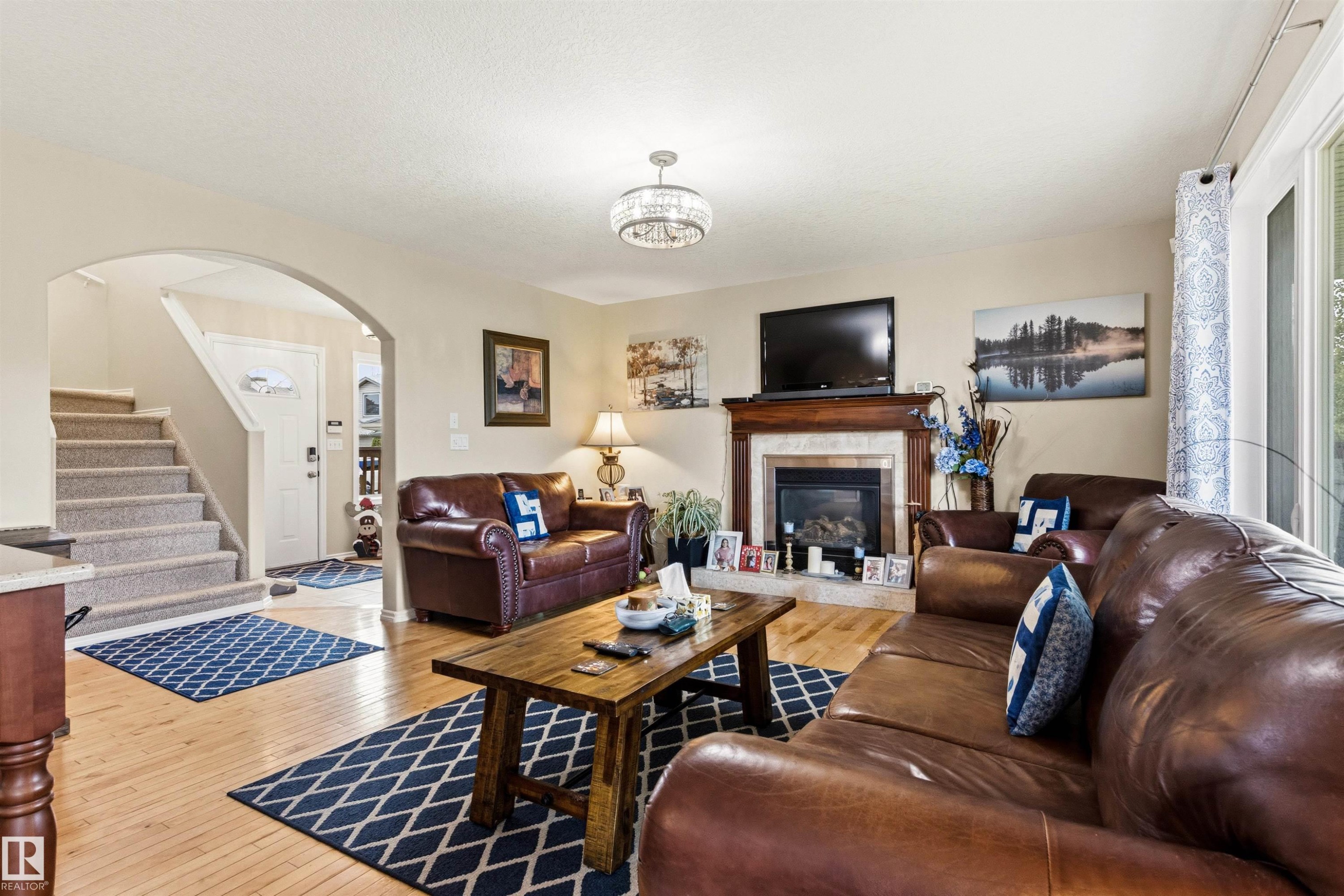 Living room featuring wood-finish flooring, a fireplace with a wood mantel and stone surround, and an arched entryway - 32 Lamplight Bay, Spruce Grove, AB