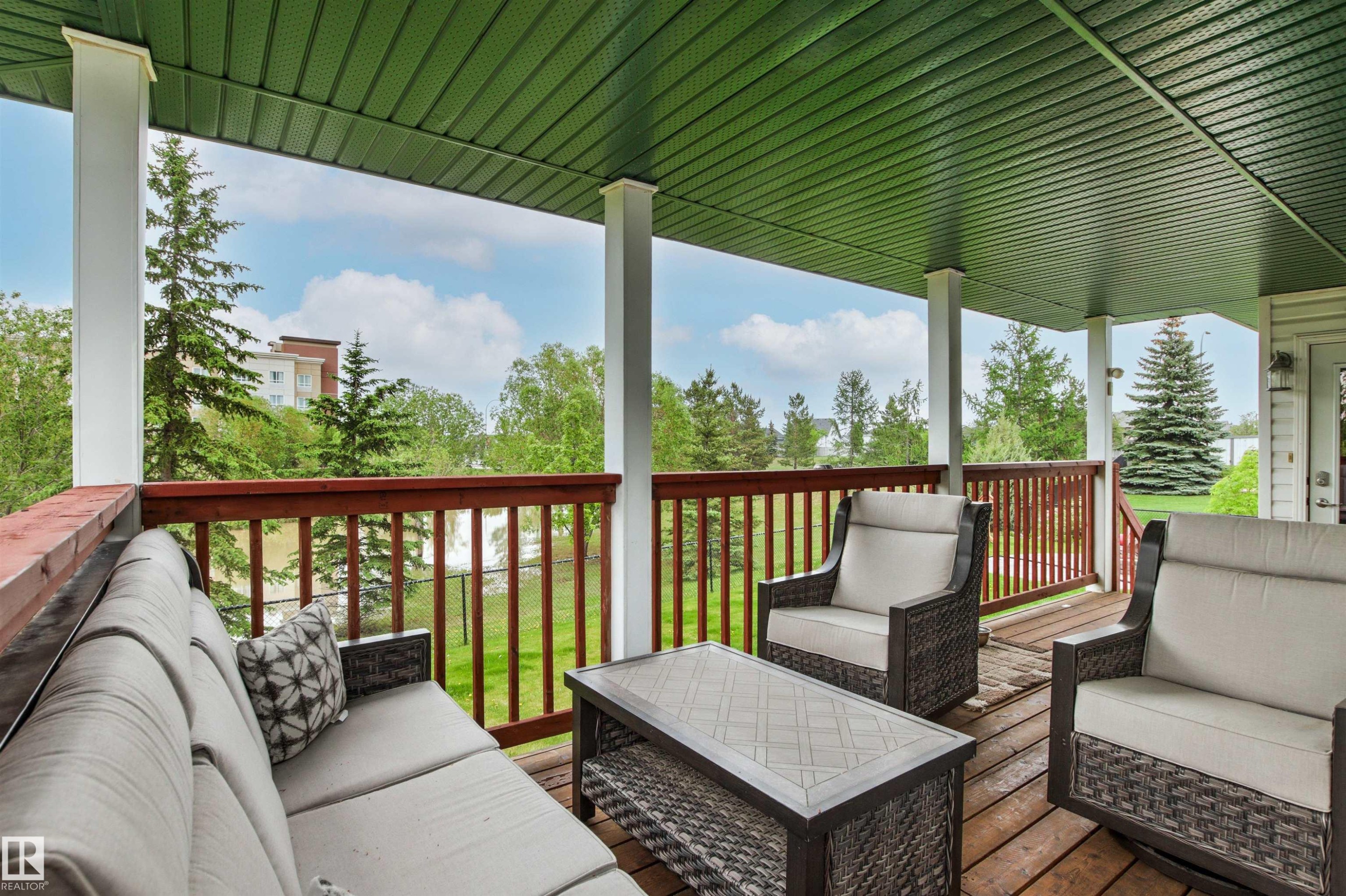 Spacious covered deck featuring wood decking, white support columns, and a rich wood railing - 32 Lamplight Bay, Spruce Grove, AB