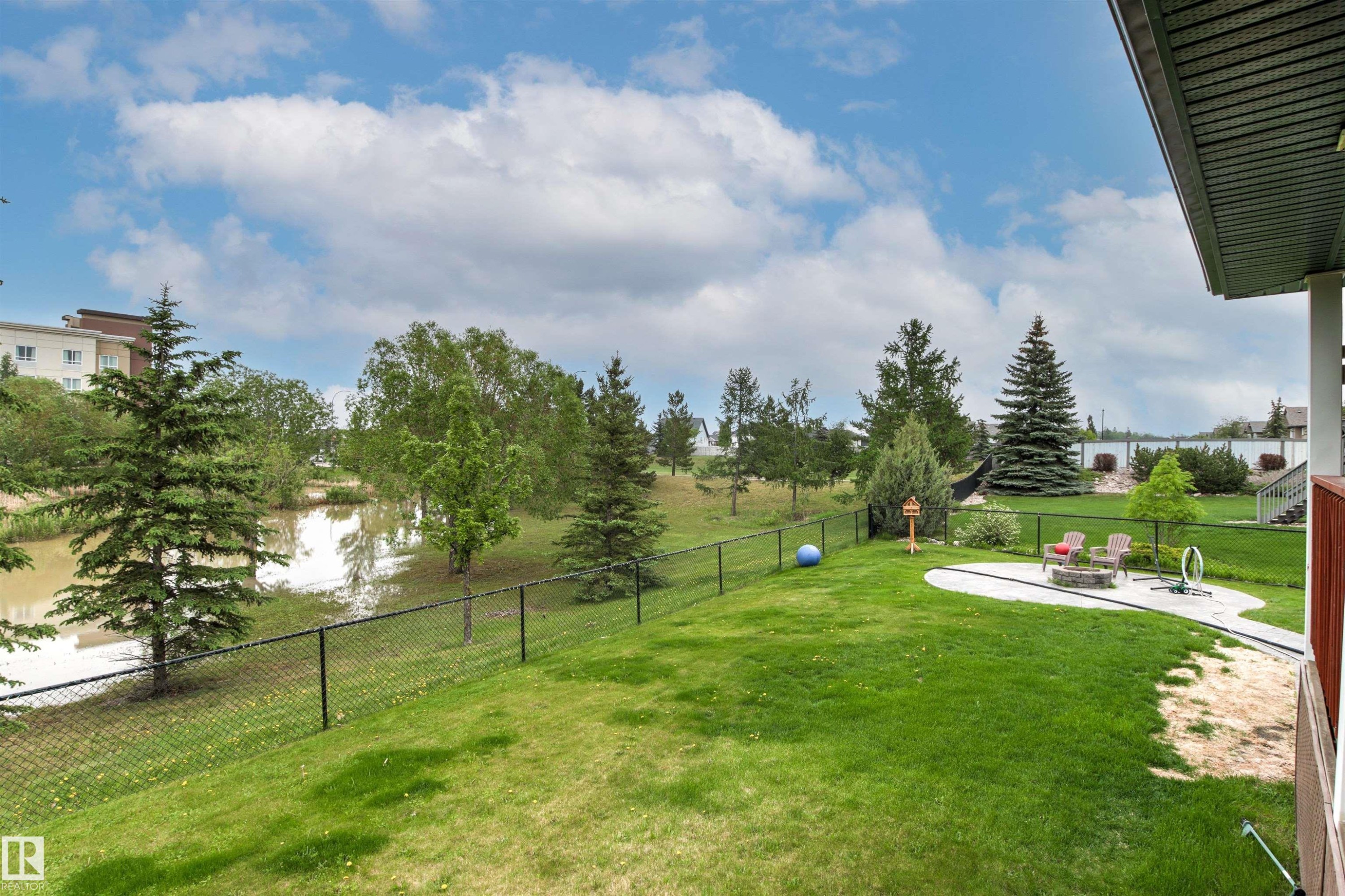 Expansive backyard featuring a manicured lawn, a concrete patio area, and mature evergreen trees - 32 Lamplight Bay, Spruce Grove, AB