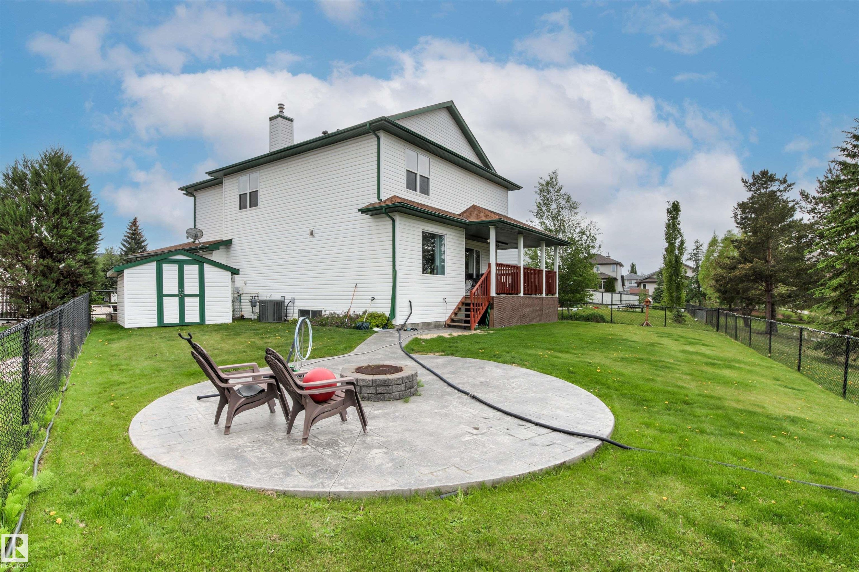 Spacious backyard featuring a circular stamped concrete patio with a built-in fire pit, a covered deck with railings, and a storage shed - 32 Lamplight Bay, Spruce Grove, AB