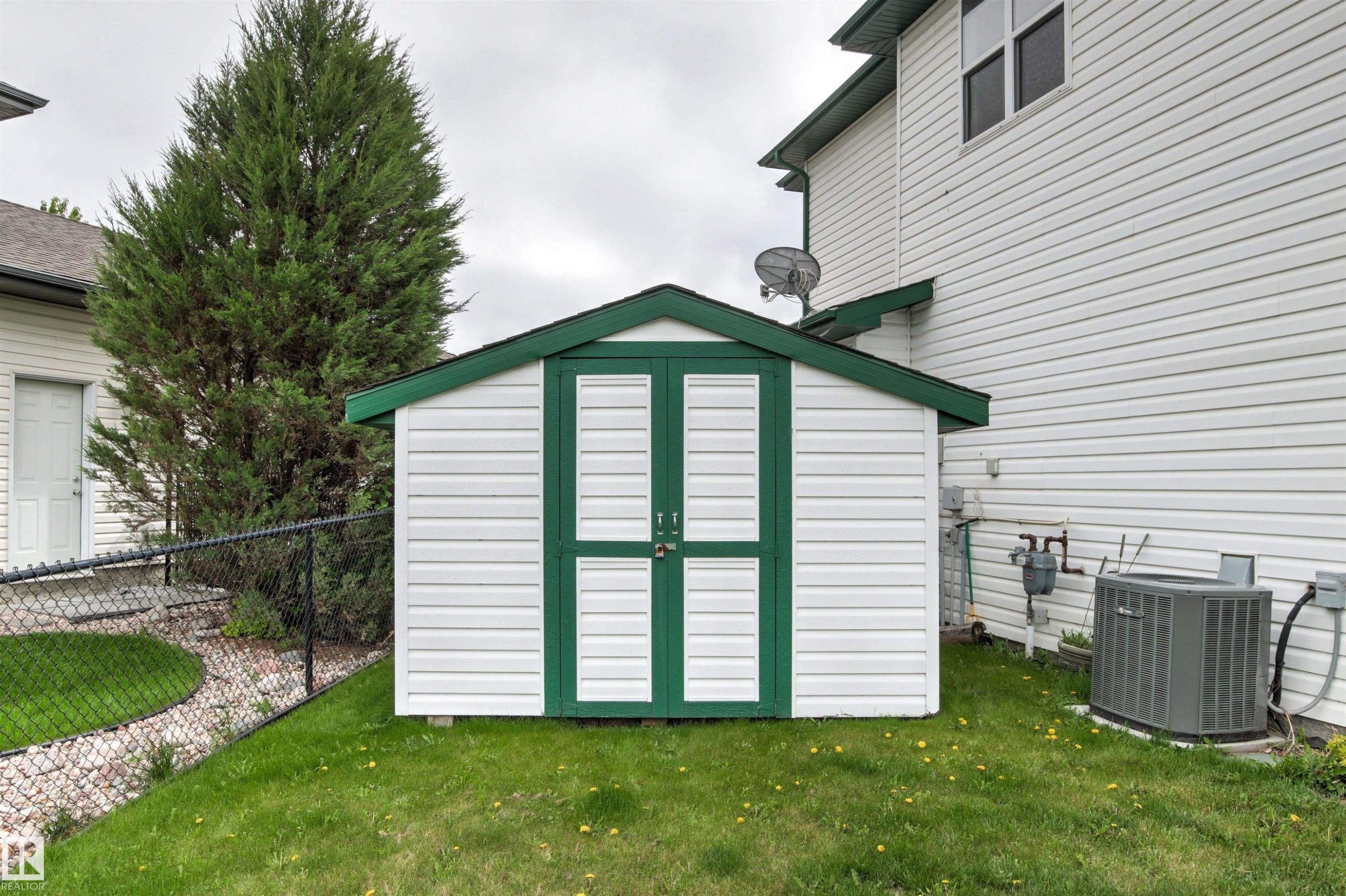 Detached storage shed featuring white siding and green trim - 32 Lamplight Bay, Spruce Grove, AB