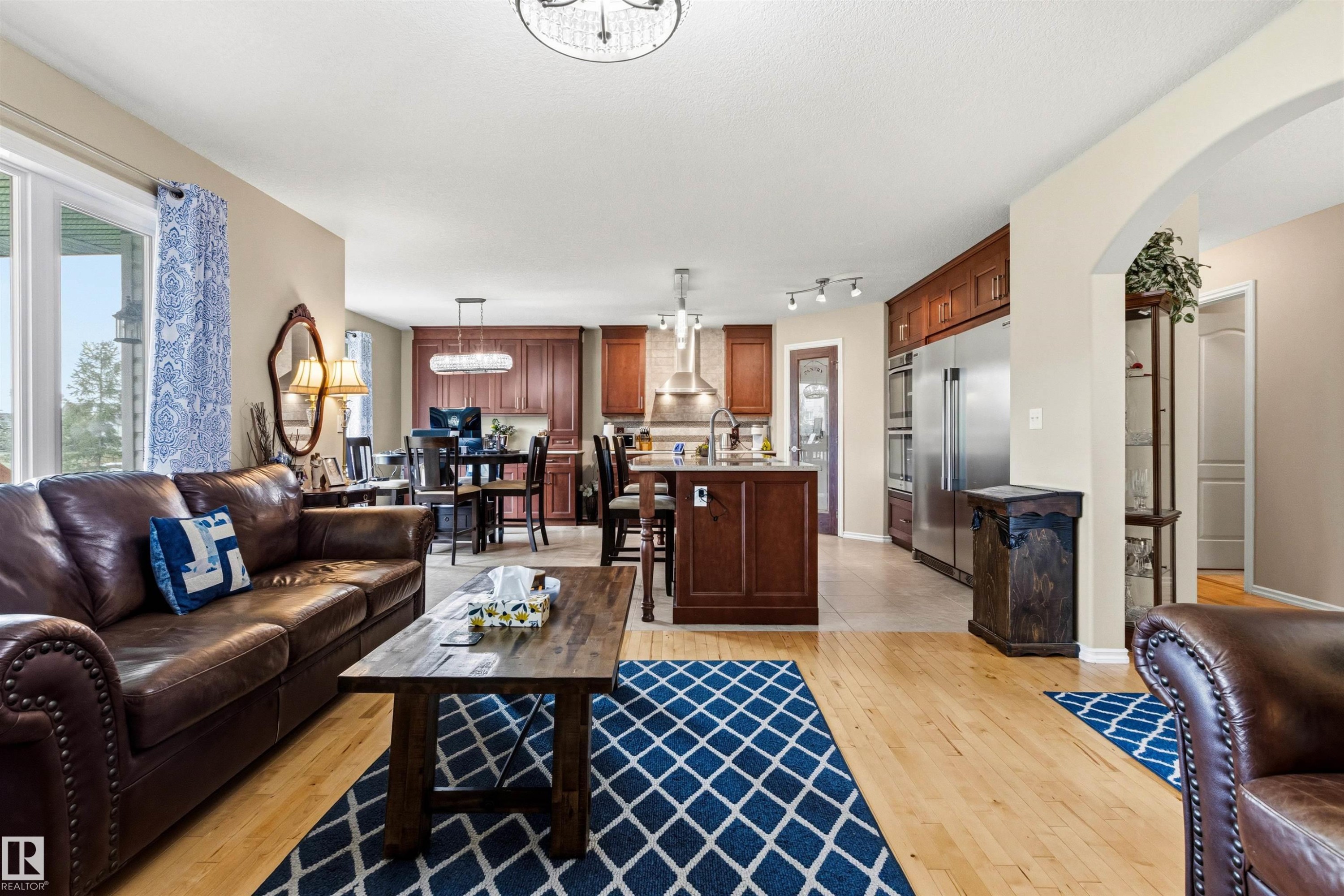 Open-concept living space featuring wood-finish flooring, a kitchen with rich wood cabinetry, stainless steel appliances, and a central island - 32 Lamplight Bay, Spruce Grove, AB