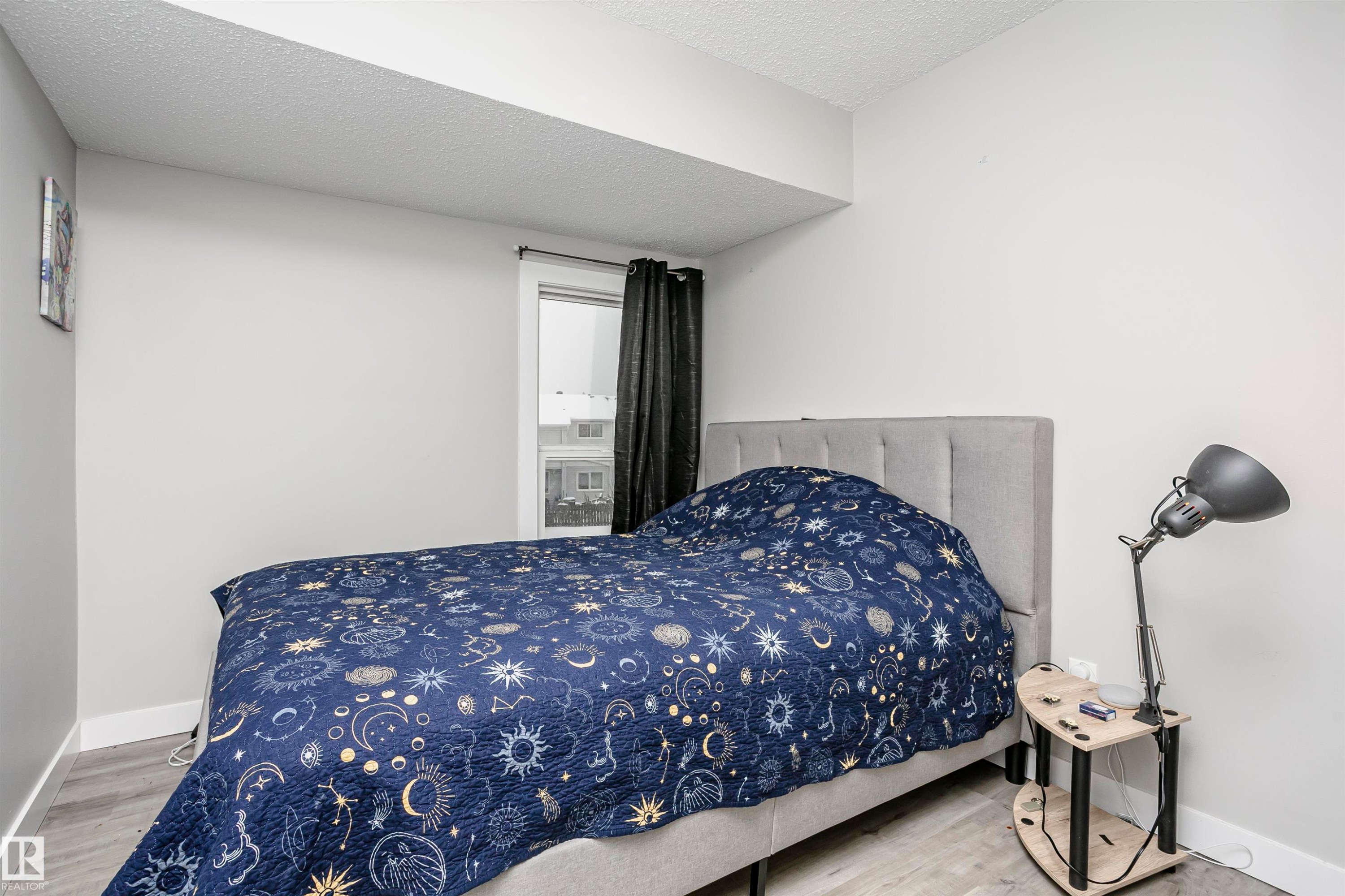 Bedroom featuring light gray walls, a window with dark curtains, and wood-finish flooring - 3103 109 Street, Edmonton, AB
