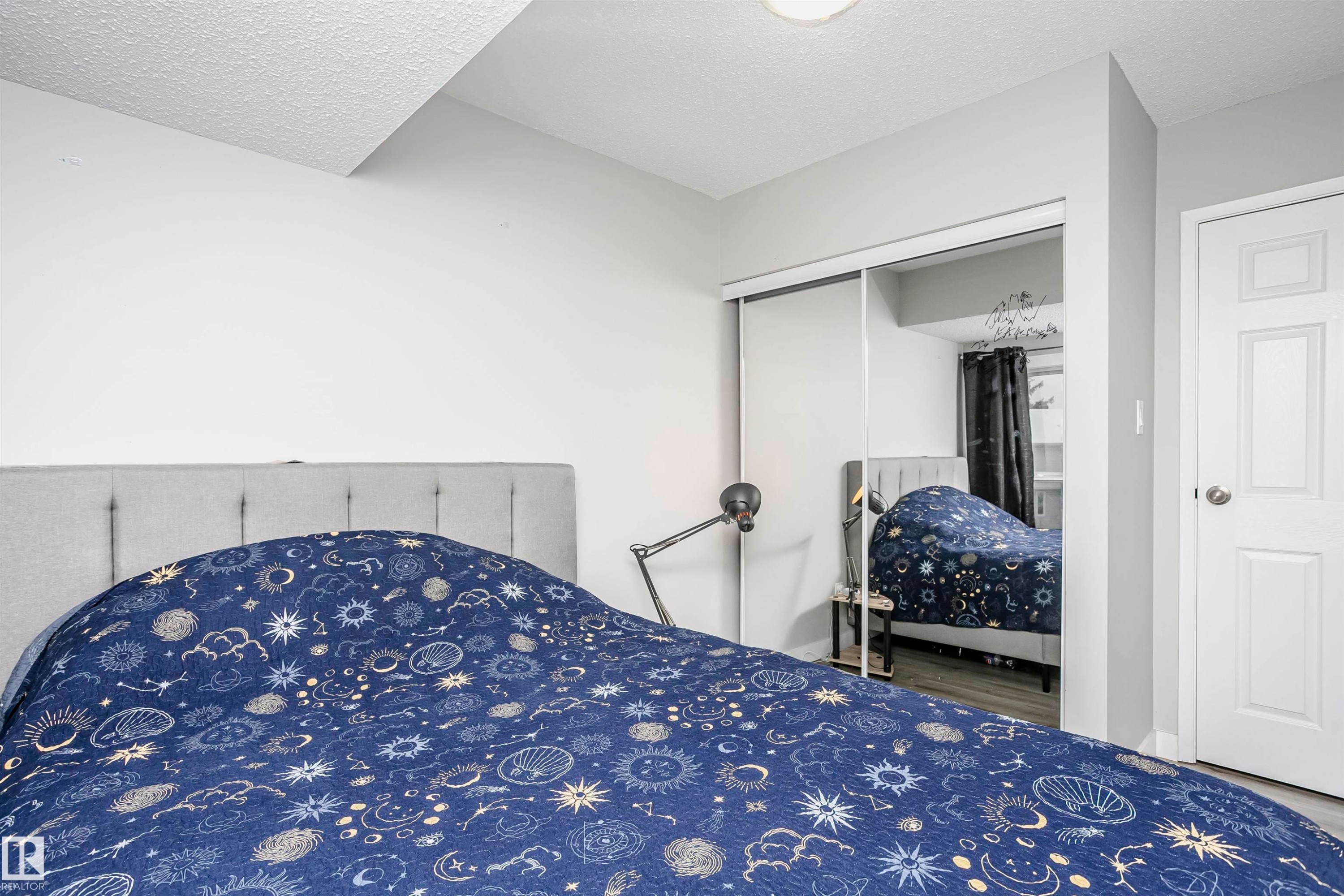 Bedroom featuring light gray walls, wood-finish flooring, a white paneled door, and mirrored sliding closet doors - 3103 109 Street, Edmonton, AB