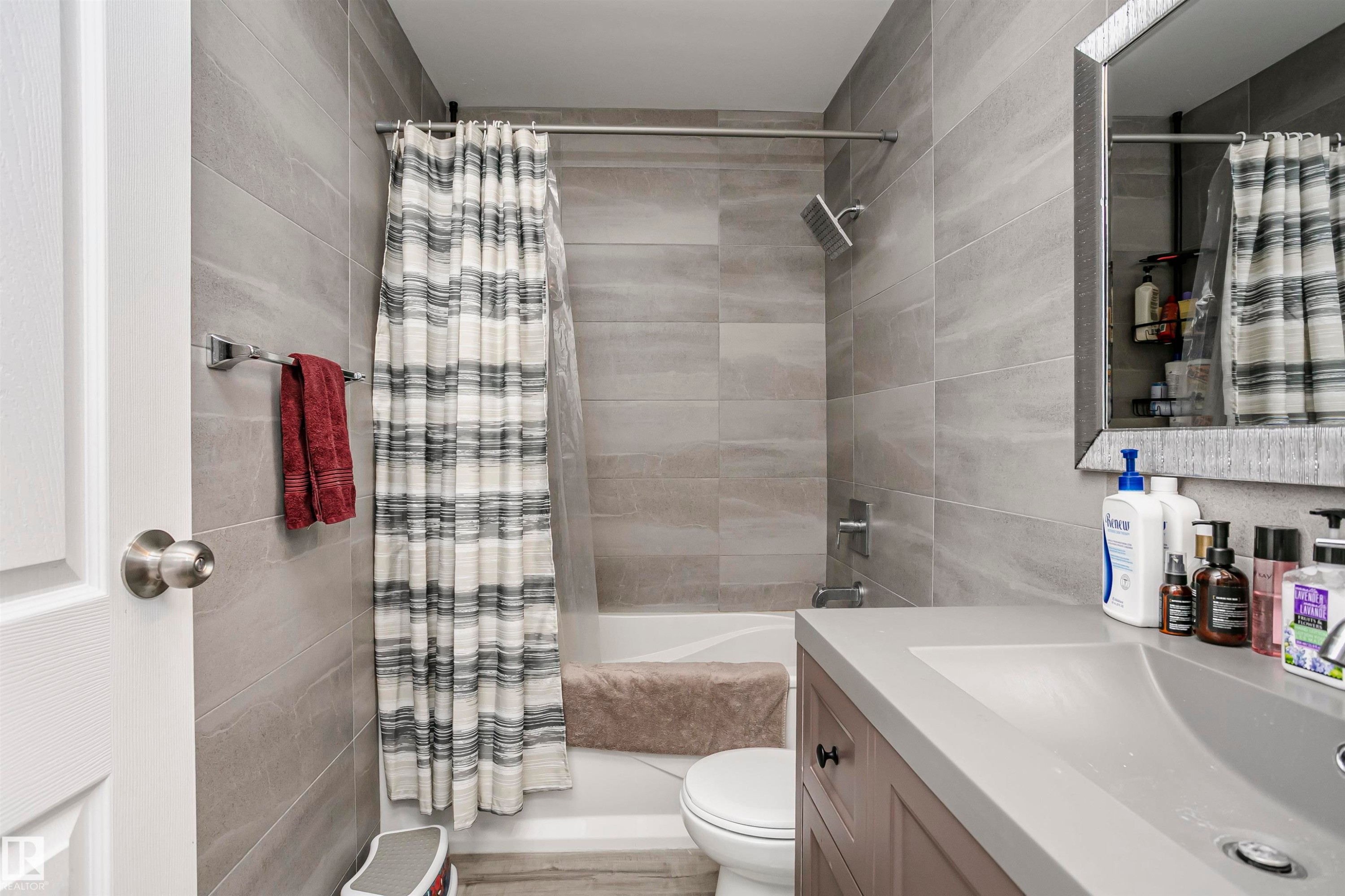 Bathroom featuring a tiled shower surround, rain shower head, integrated vanity sink, and a framed mirror - 3103 109 Street, Edmonton, AB