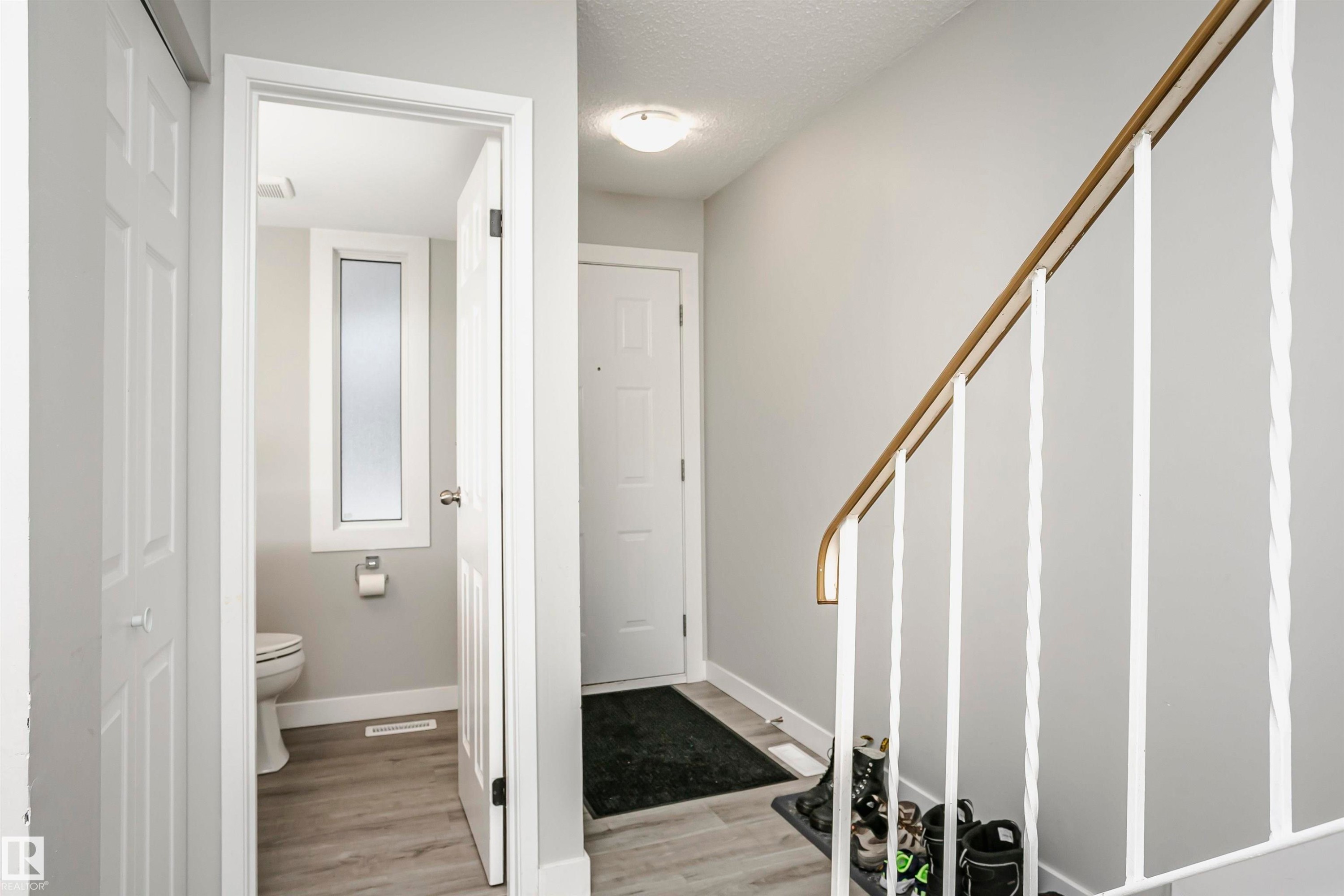 Interior hallway with light gray walls, wood-finish flooring, a white staircase with decorative balusters and a wood handrail, and a white entry door - 3103 109 Street, Edmonton, AB