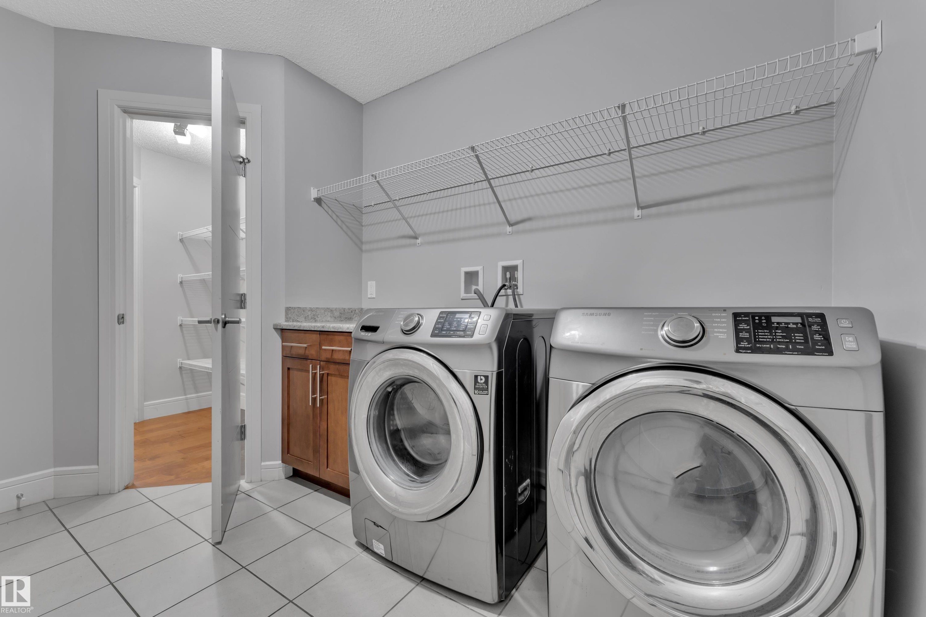 Spacious laundry area featuring tile flooring, neutral wall tones, and a built-in wire shelving system - 3363 13 Ave, Edmonton, AB