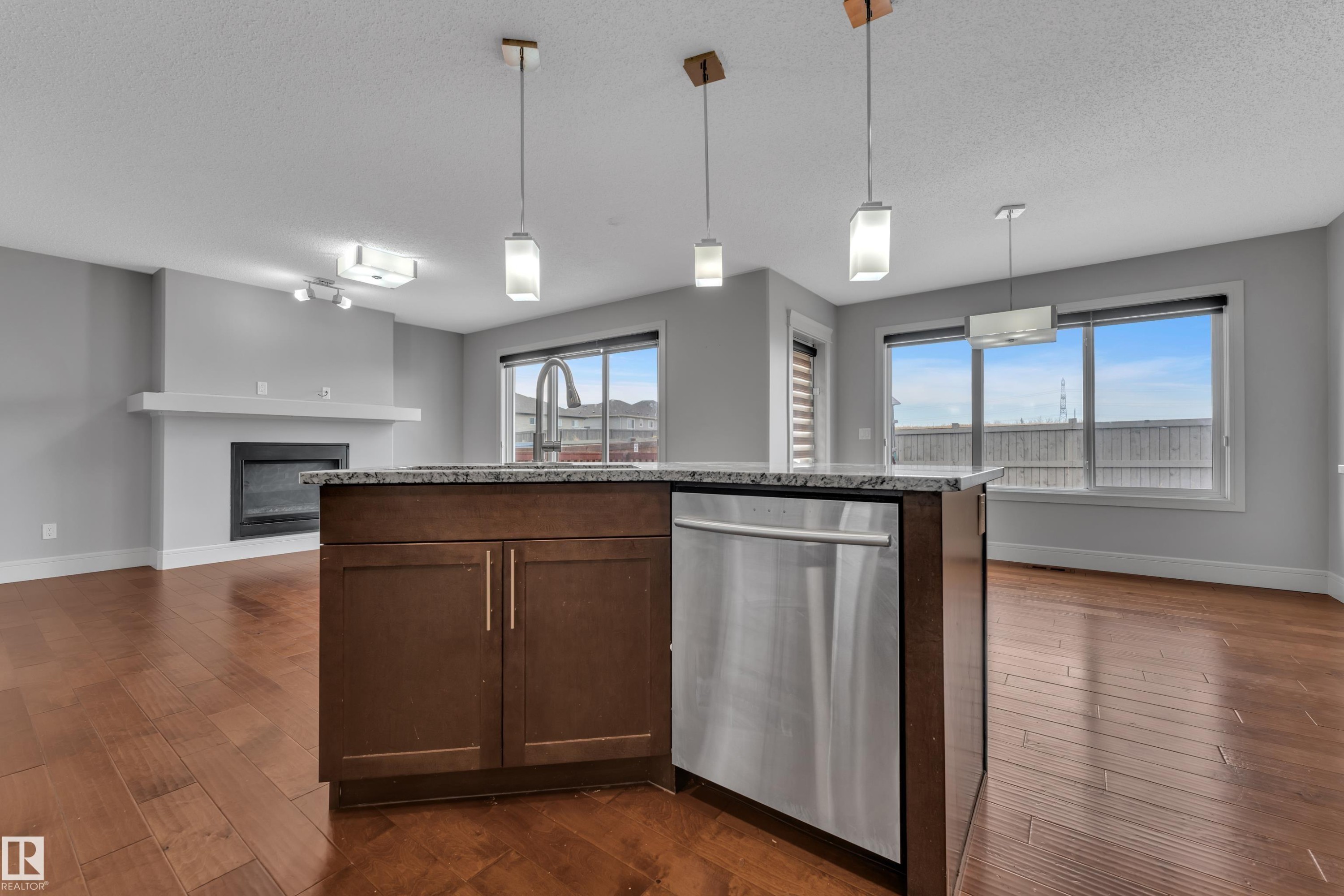 Central kitchen island featuring dark wood cabinetry, a granite-finish countertop, and an integrated stainless steel dishwasher - 3363 13 Ave, Edmonton, AB