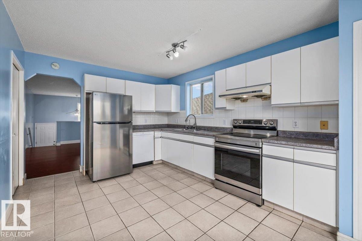 Kitchen featuring white cabinetry, stainless steel appliances, speckled countertops, ceramic tile flooring, and a tile backsplash - 8103 154 Avenue, Edmonton, AB