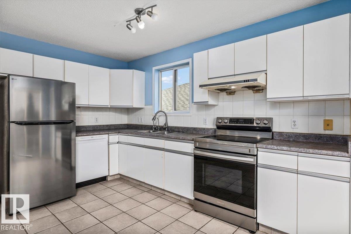 Kitchen featuring white cabinetry, tile flooring, and integrated stainless-steel appliances - 8103 154 Avenue, Edmonton, AB