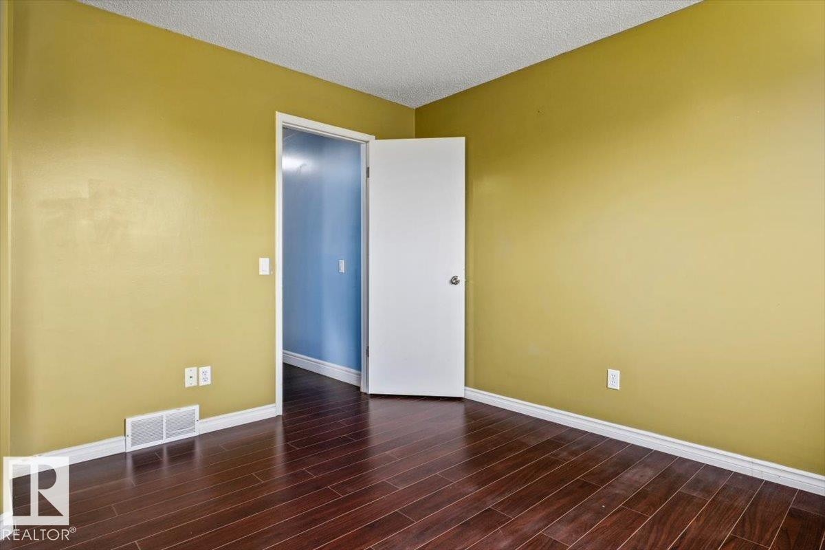 Room featuring rich wood-finish flooring, a white trim baseboard, and a white interior door - 8103 154 Avenue, Edmonton, AB
