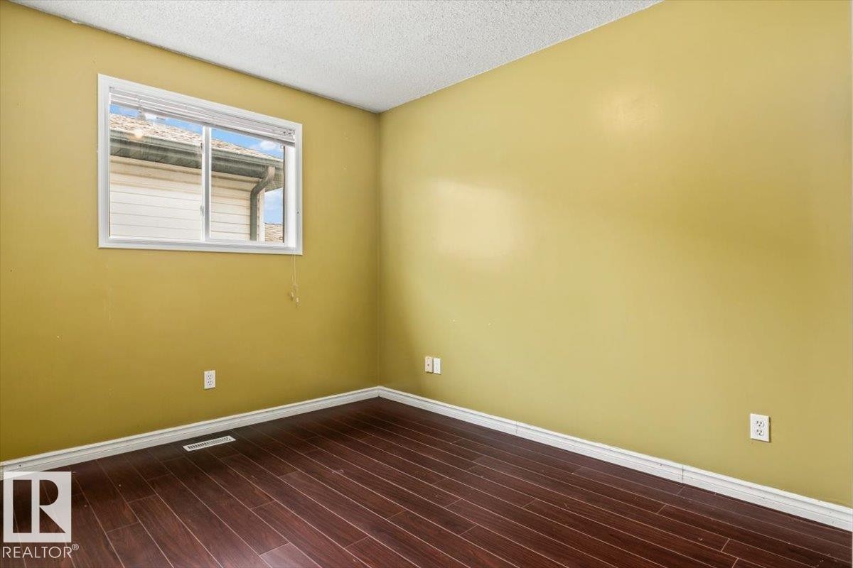 Room featuring wood-finish flooring, white baseboards, and a single window with white trim - 8103 154 Avenue, Edmonton, AB