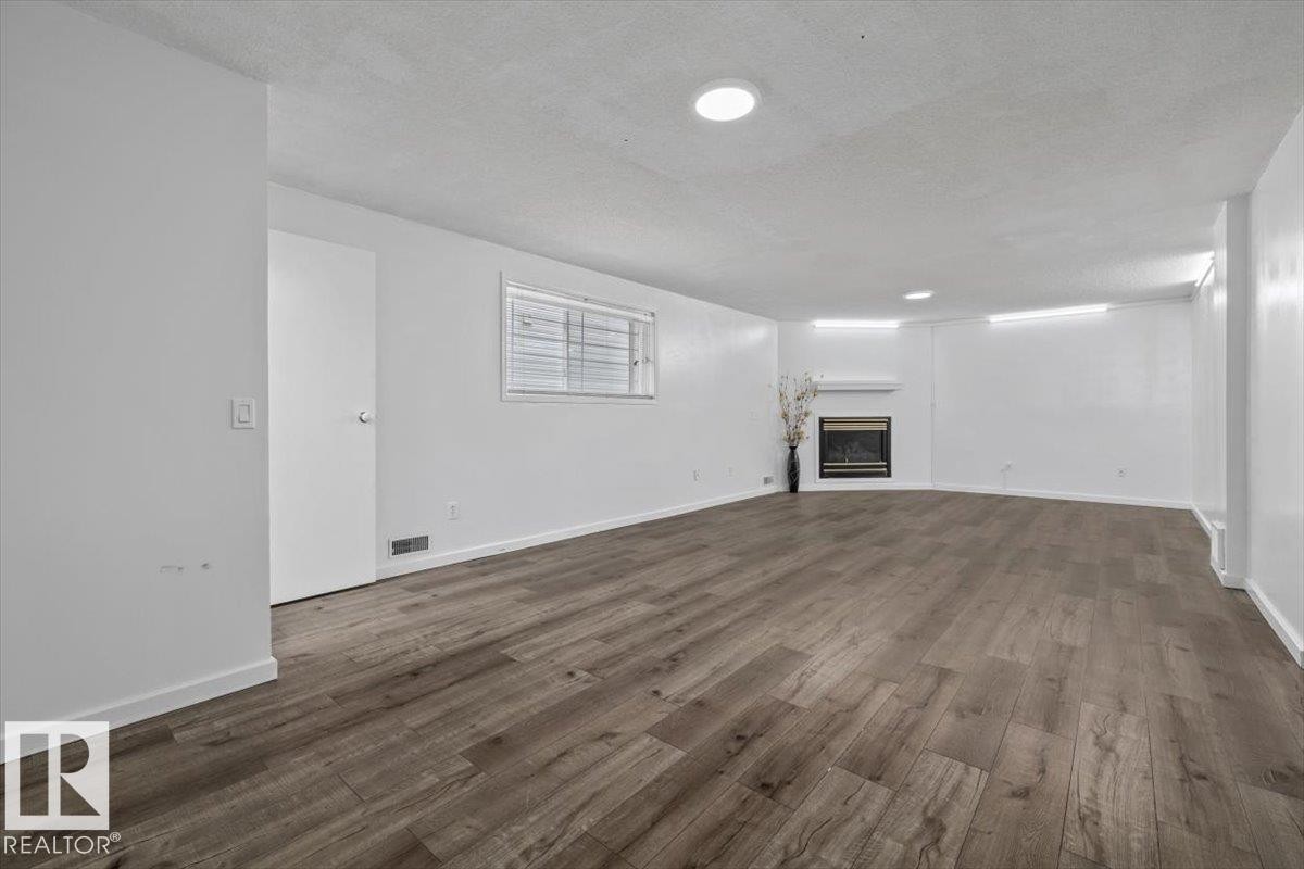 Spacious room featuring wood-finish flooring, recessed lighting, and a modern fireplace with a white mantel - 8103 154 Avenue, Edmonton, AB