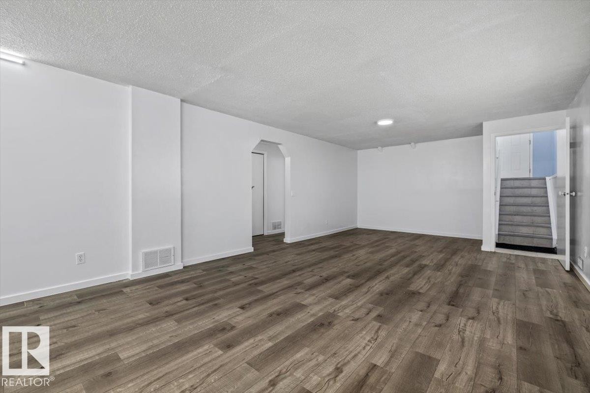 Spacious room featuring wood-finish flooring, white painted walls, white baseboards, a textured ceiling, and recessed lighting - 8103 154 Avenue, Edmonton, AB