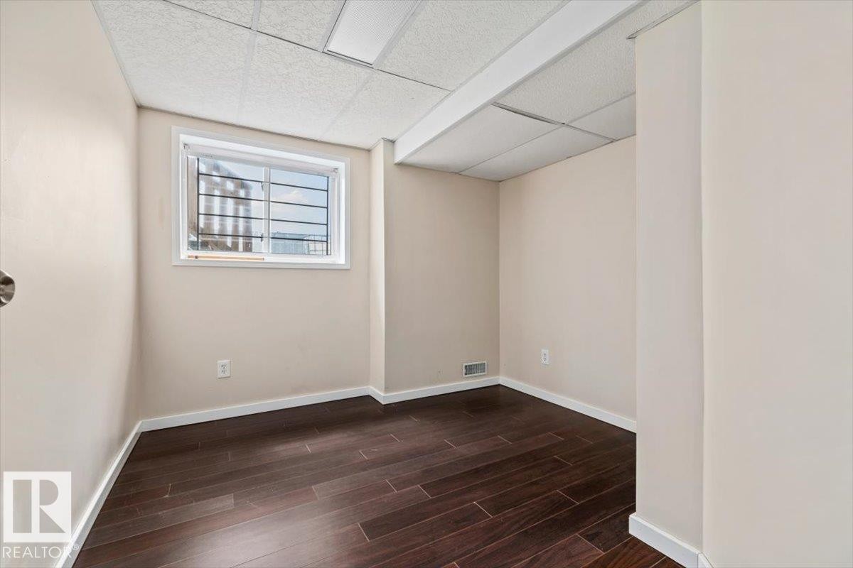 Room featuring dark wood-finish flooring, light-toned walls, and a drop ceiling with integrated lighting - 8103 154 Avenue, Edmonton, AB