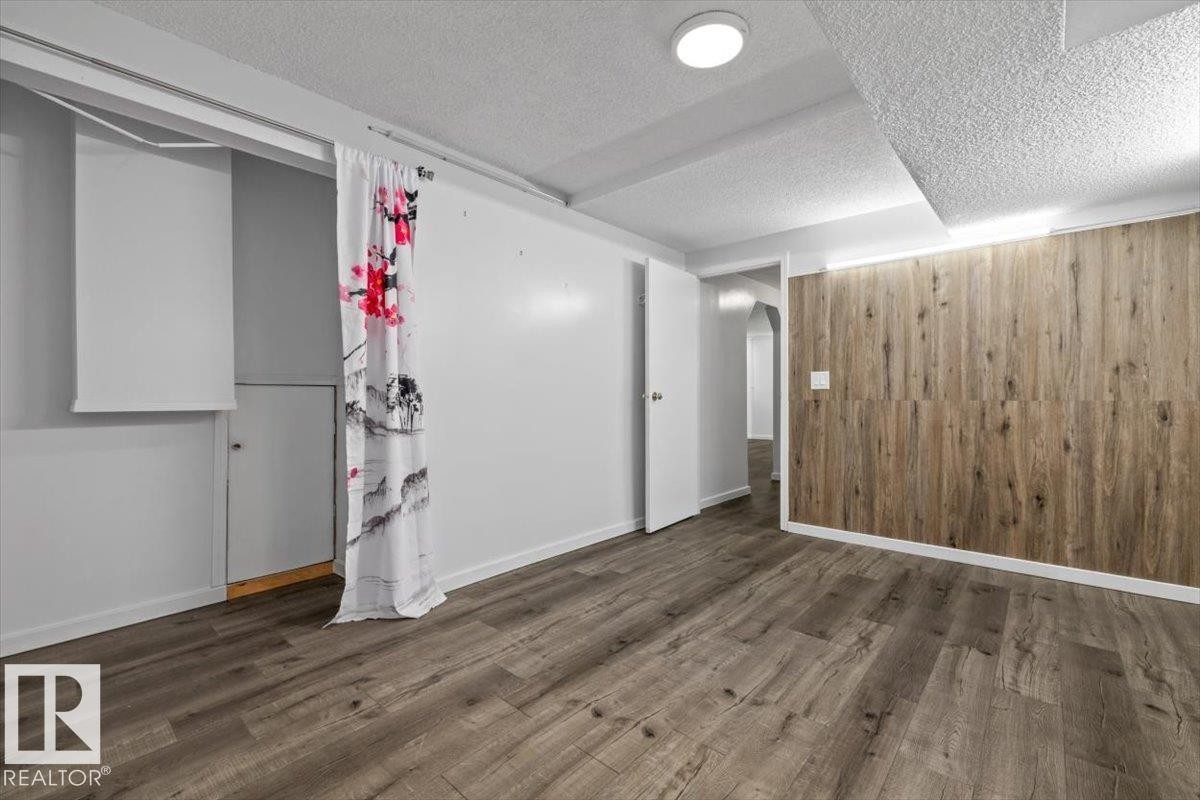 Spacious room featuring wood-finish flooring and a distinctive wood-panel accent wall - 8103 154 Avenue, Edmonton, AB
