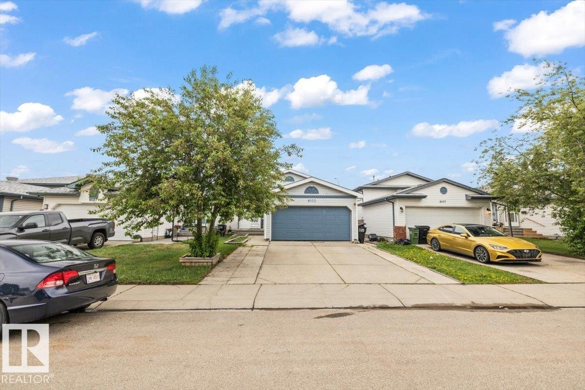 Front exterior featuring a light-colored facade, an attached two-car garage with a blue door, and a concrete driveway - 8103 154 Avenue, Edmonton, AB