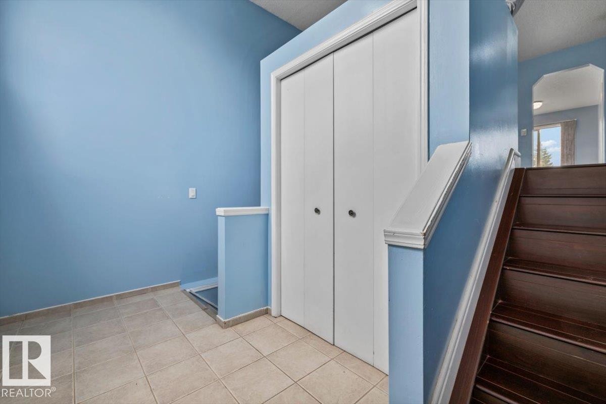 Foyer featuring large format tile flooring, a double-door closet, and dark wood-finish stairs with a coordinating banister - 8103 154 Avenue, Edmonton, AB