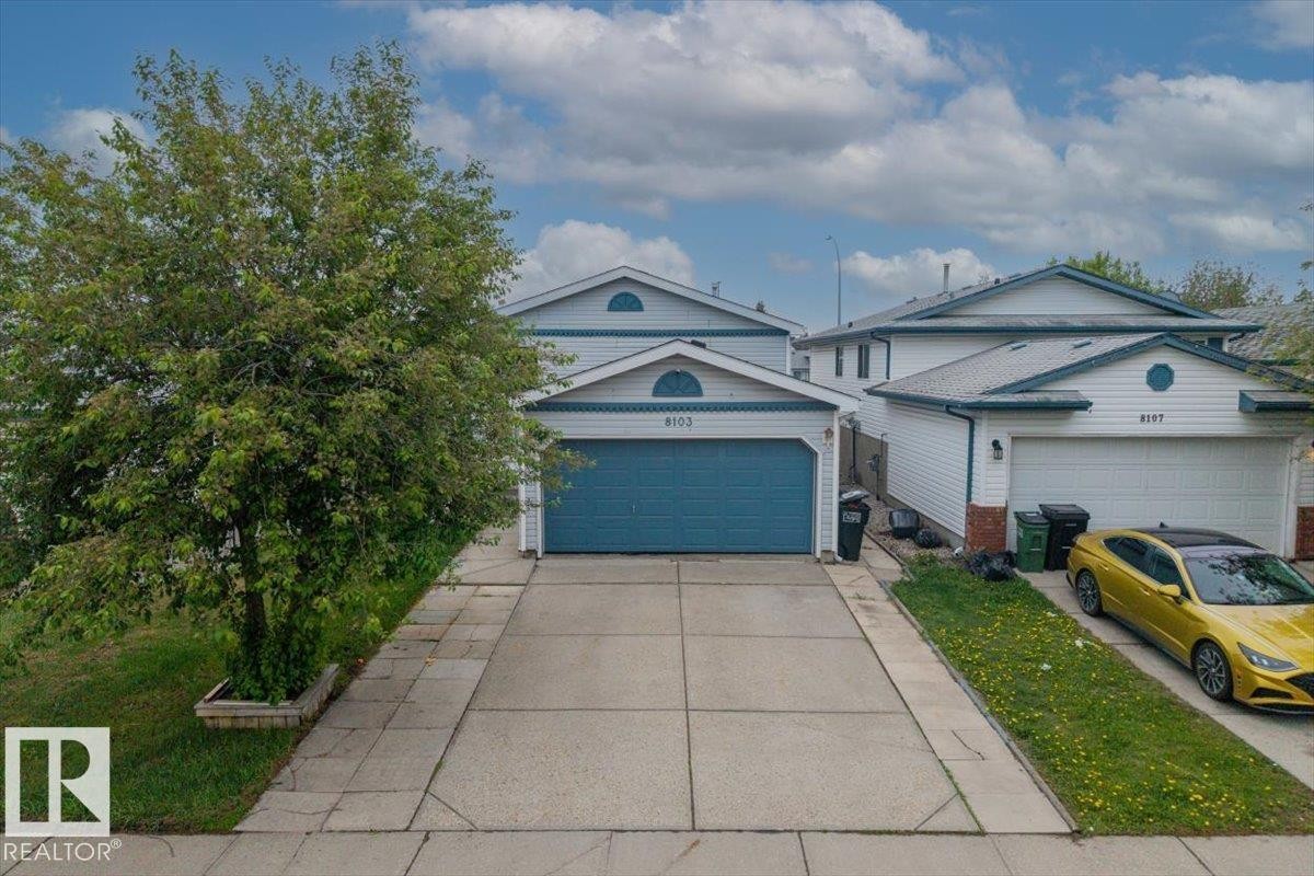 Front exterior featuring a blue garage door, white siding, and an arched gable accent - 8103 154 Avenue, Edmonton, AB