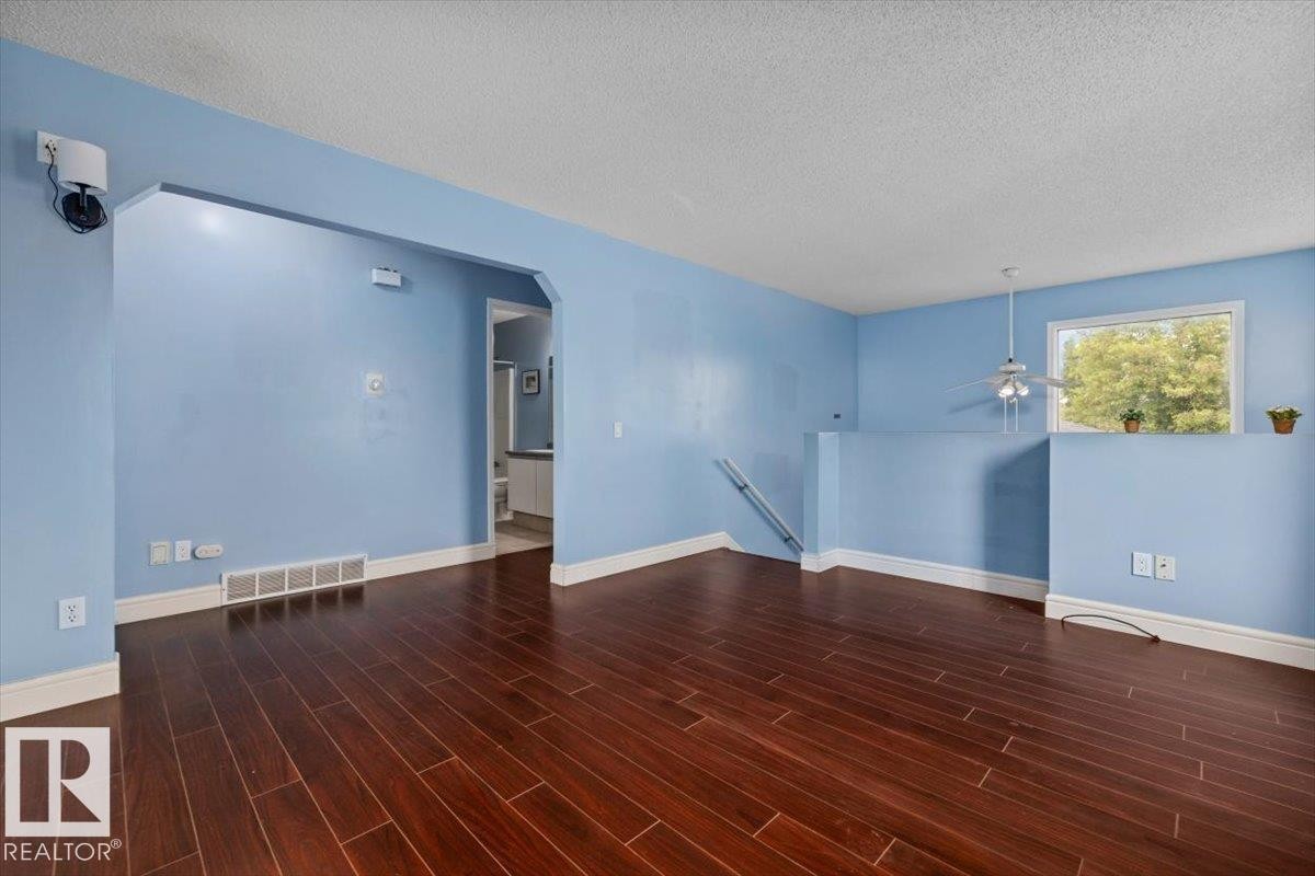 Spacious interior featuring rich wood-finish flooring, an arched doorway, and a ceiling fan with integrated lighting - 8103 154 Avenue, Edmonton, AB