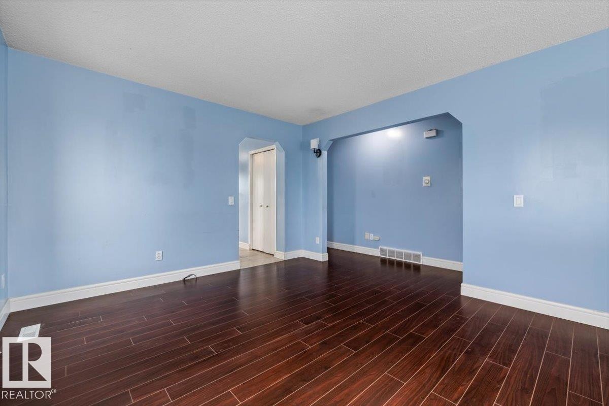Spacious room featuring rich wood-finish flooring, light blue walls, white trim, and an arched doorway - 8103 154 Avenue, Edmonton, AB