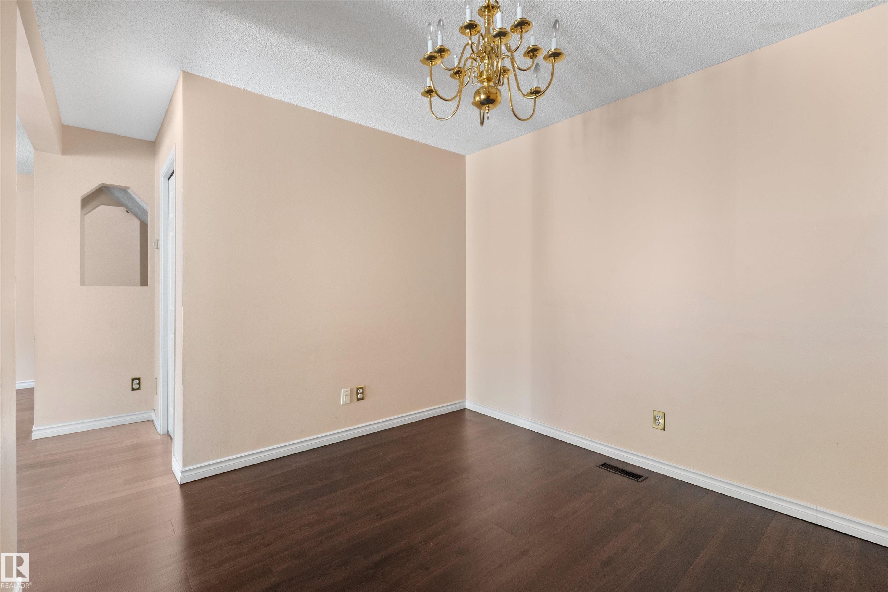 Spacious room featuring dark wood-finish flooring, light-toned walls, and a gold-tone chandelier - 5 20 Deerbourne Drive, St. Albert, AB