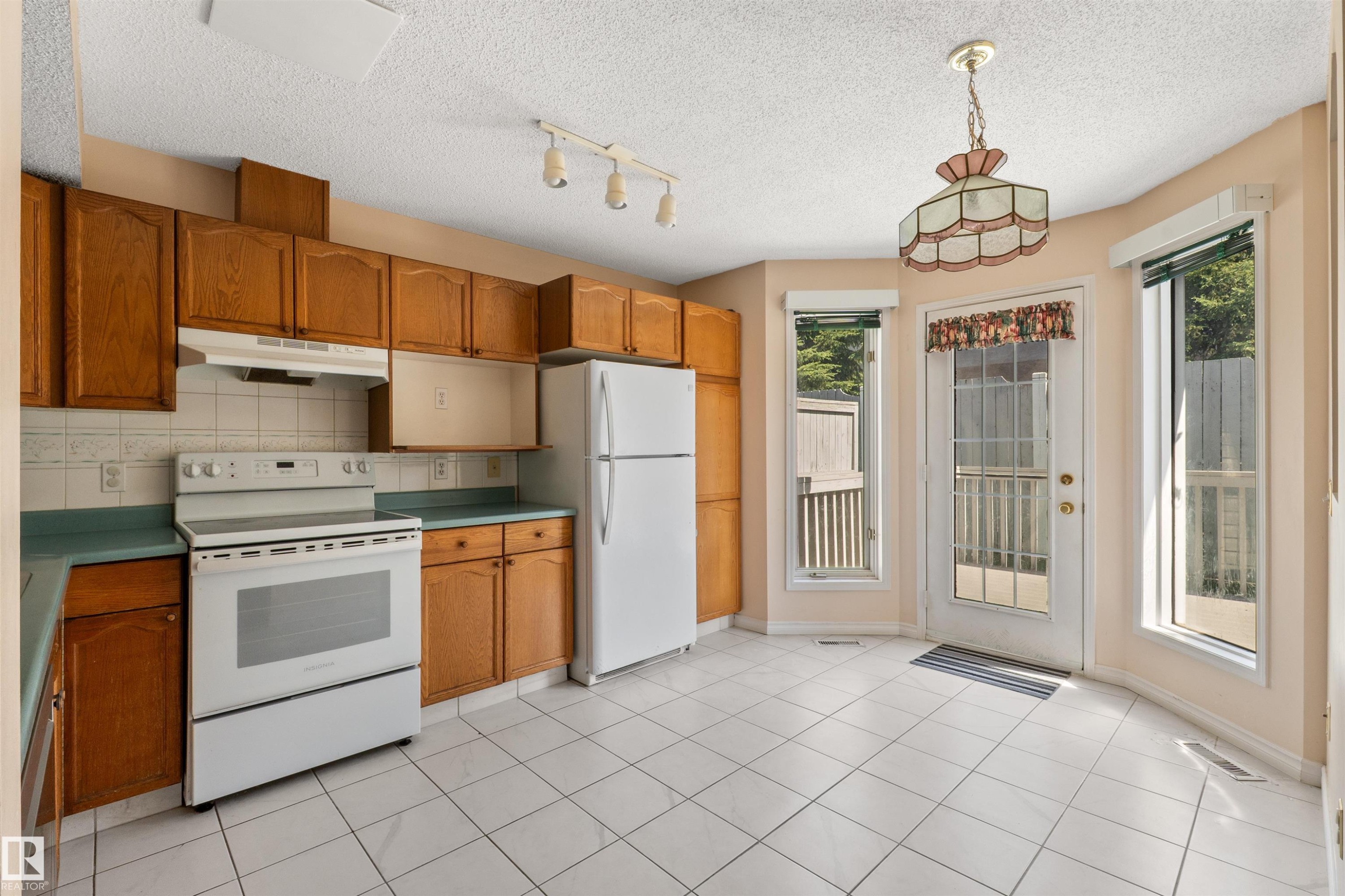 Kitchen featuring wood cabinetry, white appliances, white tile flooring, and a glass-paneled door with surrounding windows - 5 20 Deerbourne Drive, St. Albert, AB