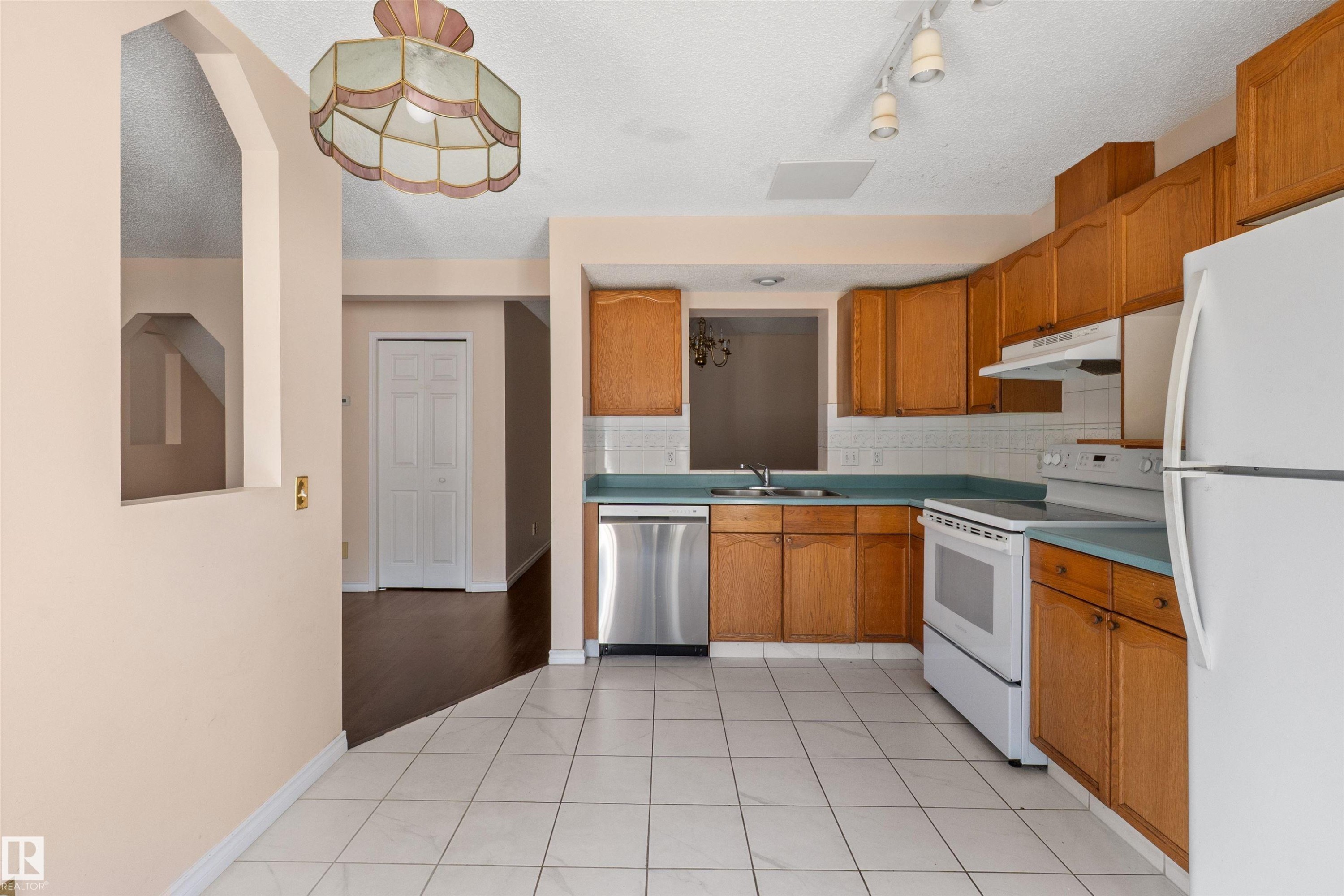 Kitchen featuring wood-finish cabinetry, white tile flooring, white appliances, and a stainless steel dishwasher - 5 20 Deerbourne Drive, St. Albert, AB