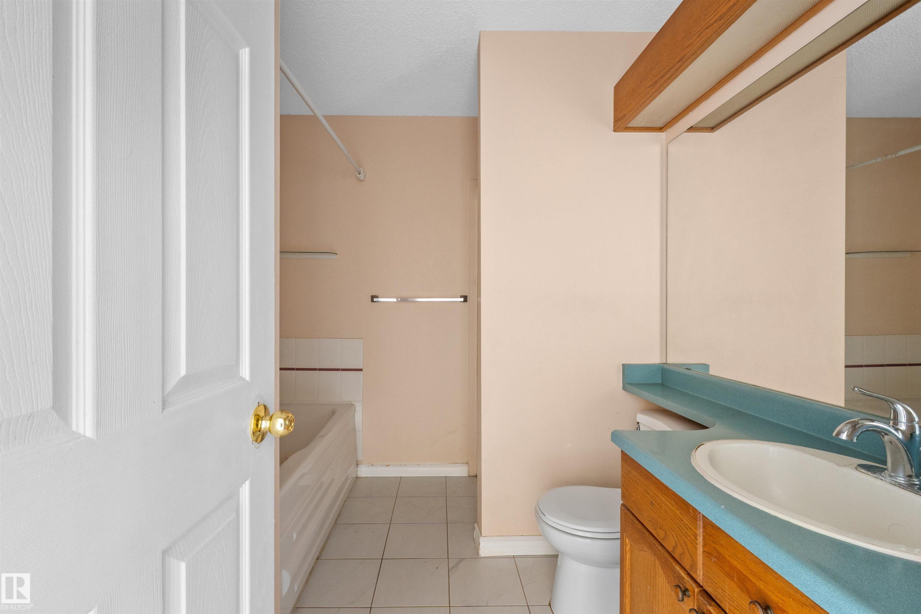 Bathroom featuring a built-in bathtub, a vanity with a white basin and blue countertop, a toilet, and tiled flooring - 5 20 Deerbourne Drive, St. Albert, AB