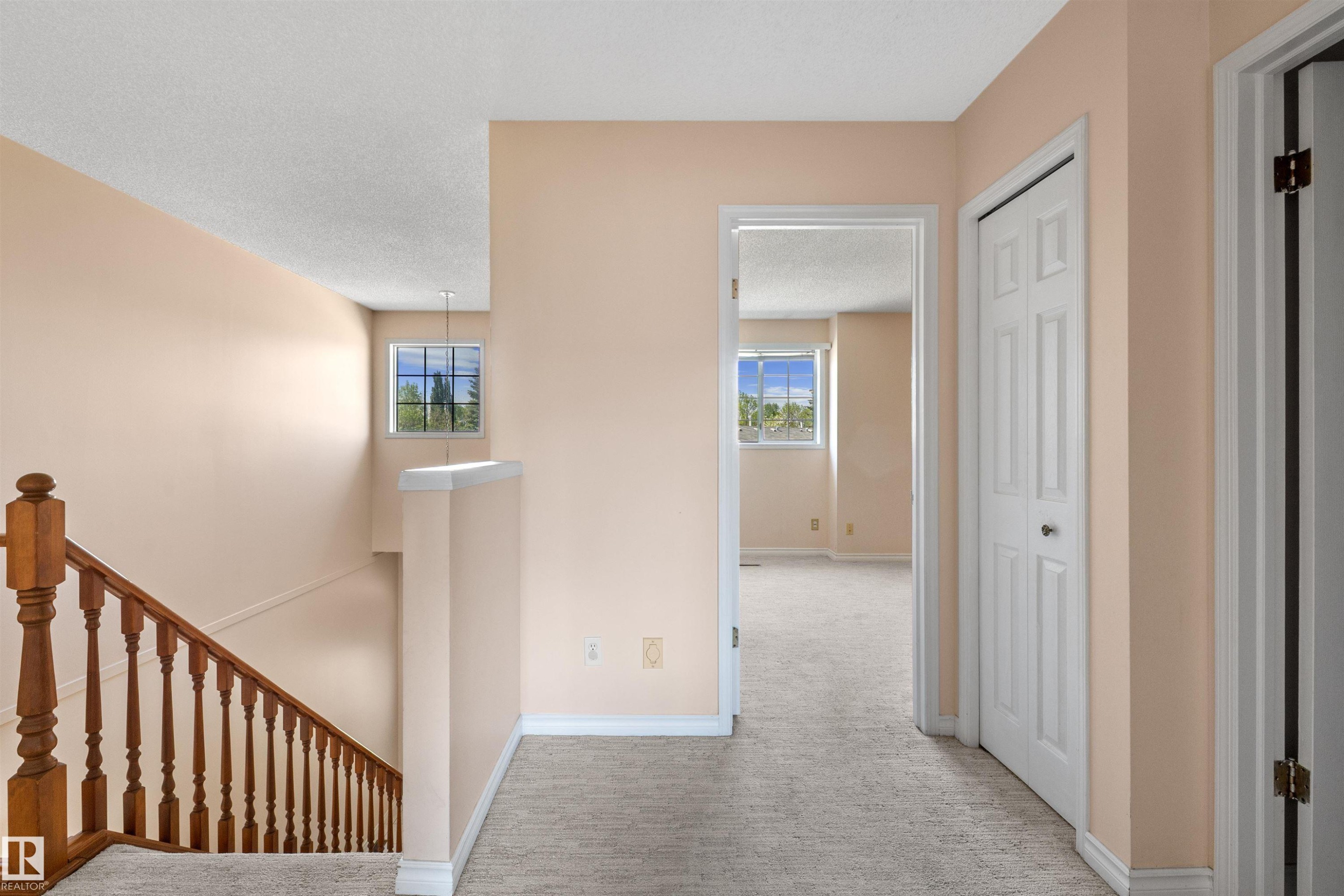 Upper level hallway featuring a wood staircase with balusters, light-colored carpeting, white baseboards, and a paneled closet door - 5 20 Deerbourne Drive, St. Albert, AB
