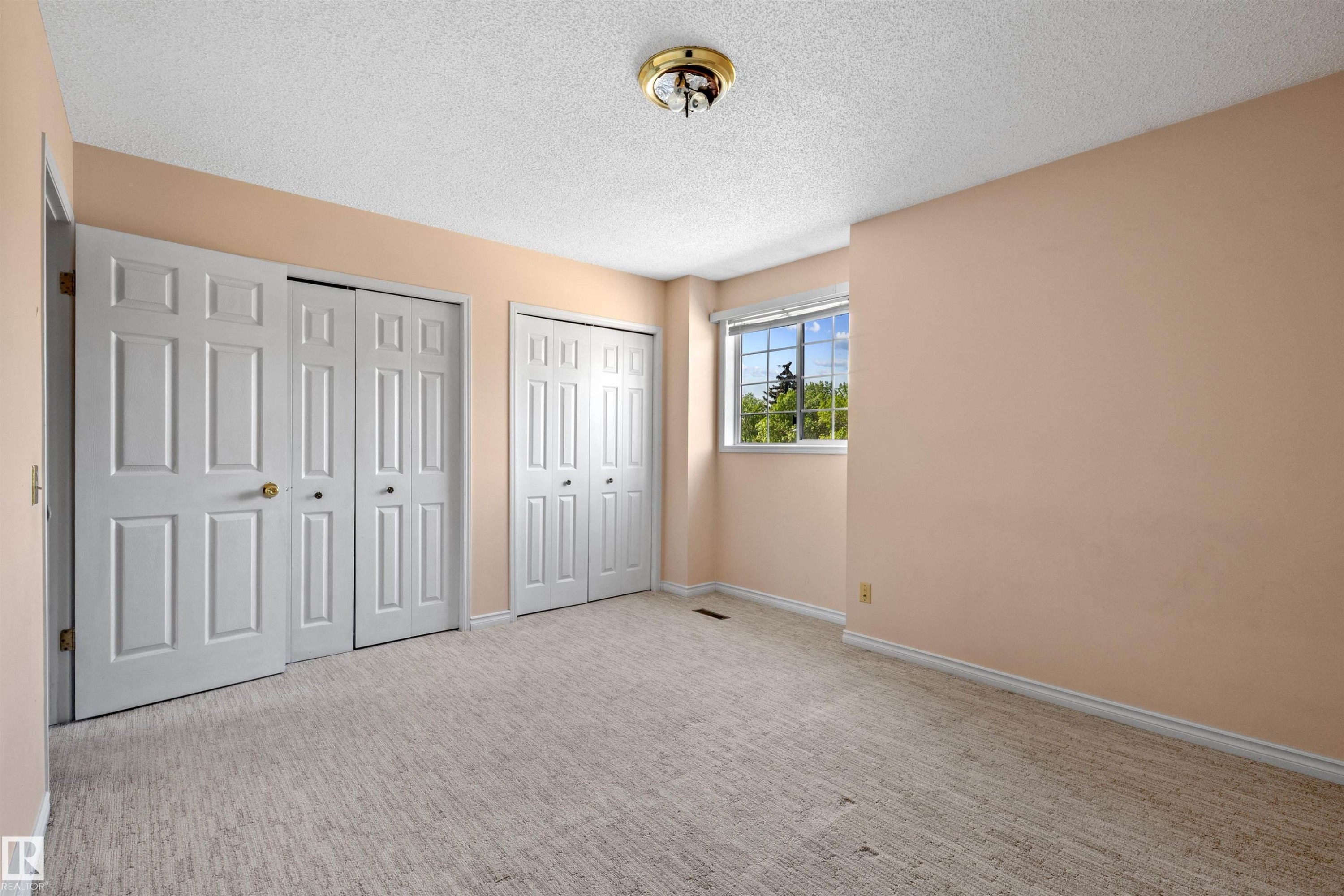 Carpeted room featuring multiple panel doors, a ceiling-mounted light fixture, and a window with exterior visibility - 5 20 Deerbourne Drive, St. Albert, AB