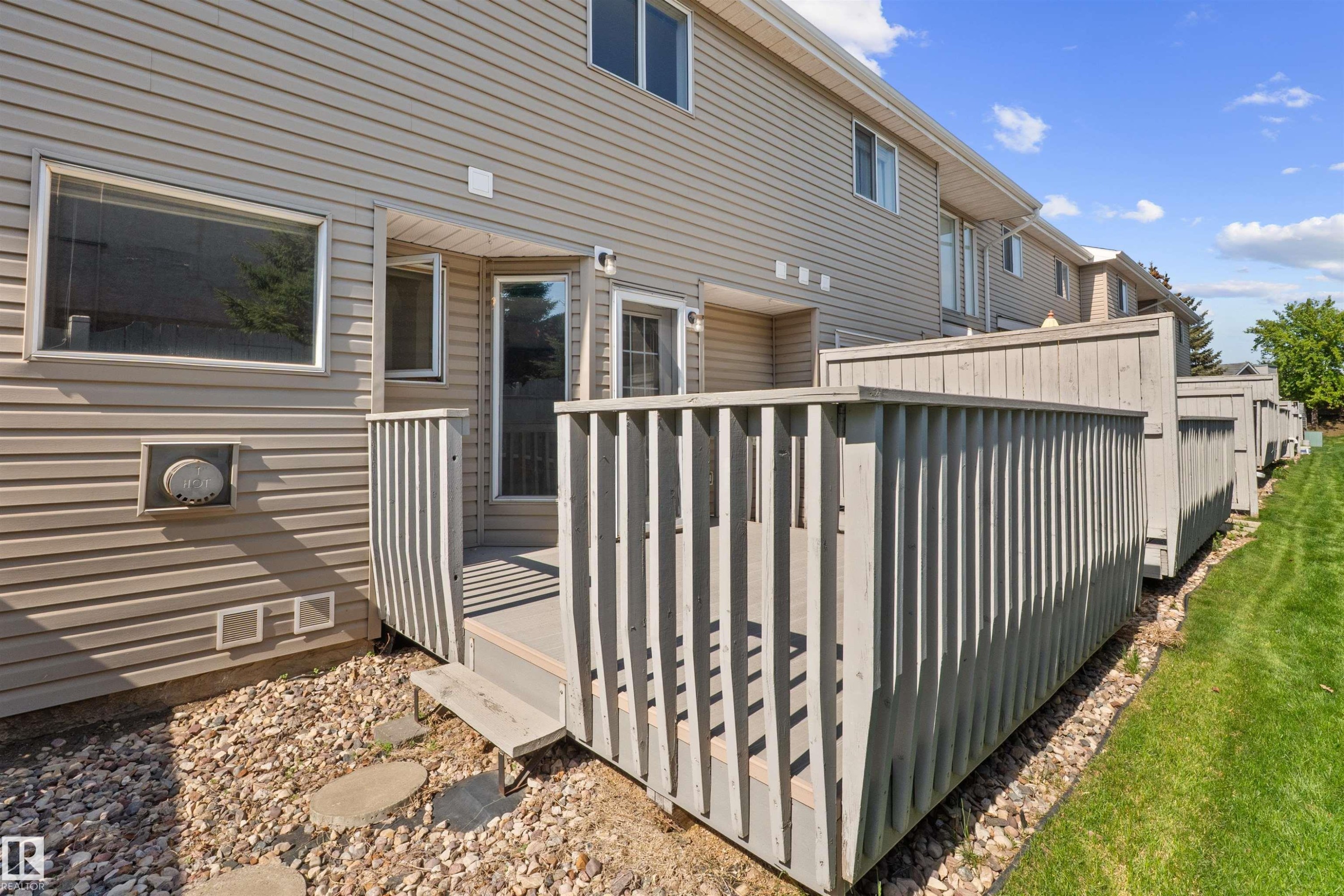 Rear exterior featuring a private deck with slatted railings, a sliding glass door, and a ground-level window - 5 20 Deerbourne Drive, St. Albert, AB