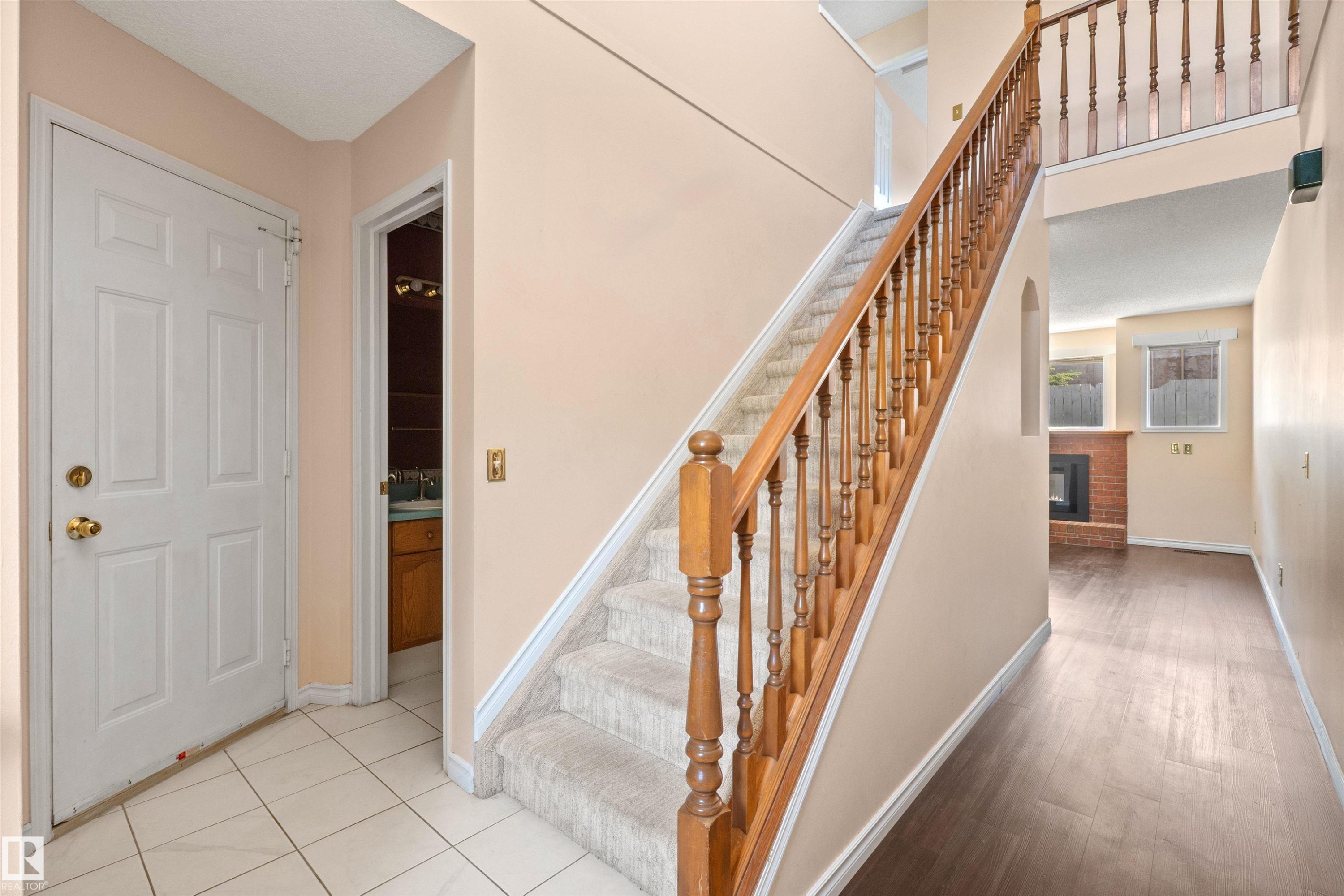 Entry foyer featuring white ceramic tile flooring and a view of the carpeted staircase with wood banister - 5 20 Deerbourne Drive, St. Albert, AB