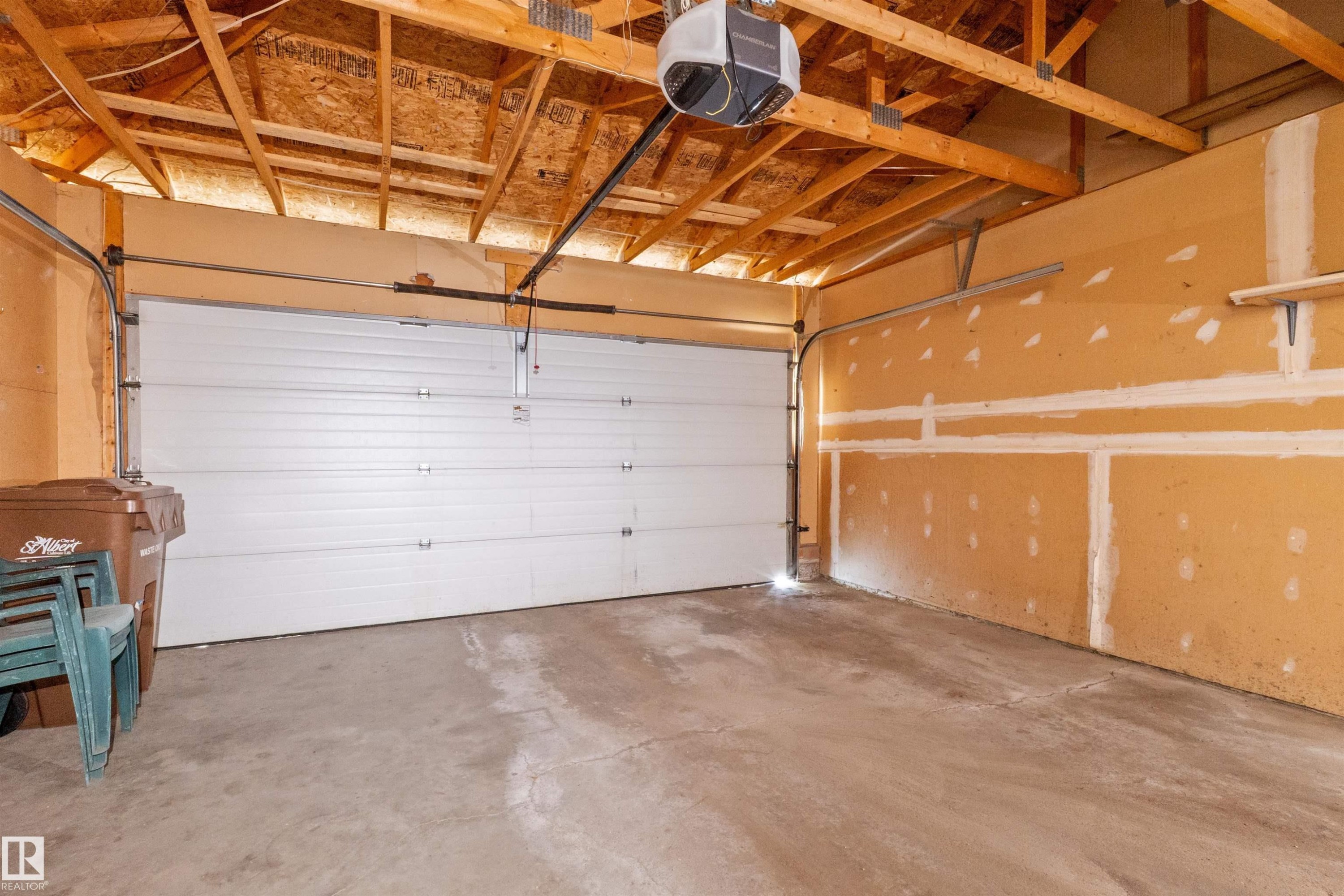 Spacious garage with a sectional overhead door, concrete flooring, exposed wooden ceiling trusses, and an automatic garage door opener - 5 20 Deerbourne Drive, St. Albert, AB
