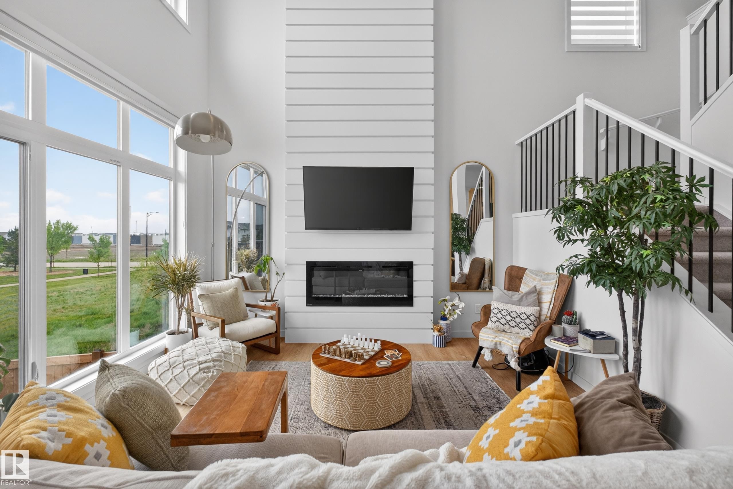 Two-story living area featuring a shiplap fireplace surround, floor-to-ceiling windows, and a staircase with open black spindles - 17023 45 Street, Edmonton, AB